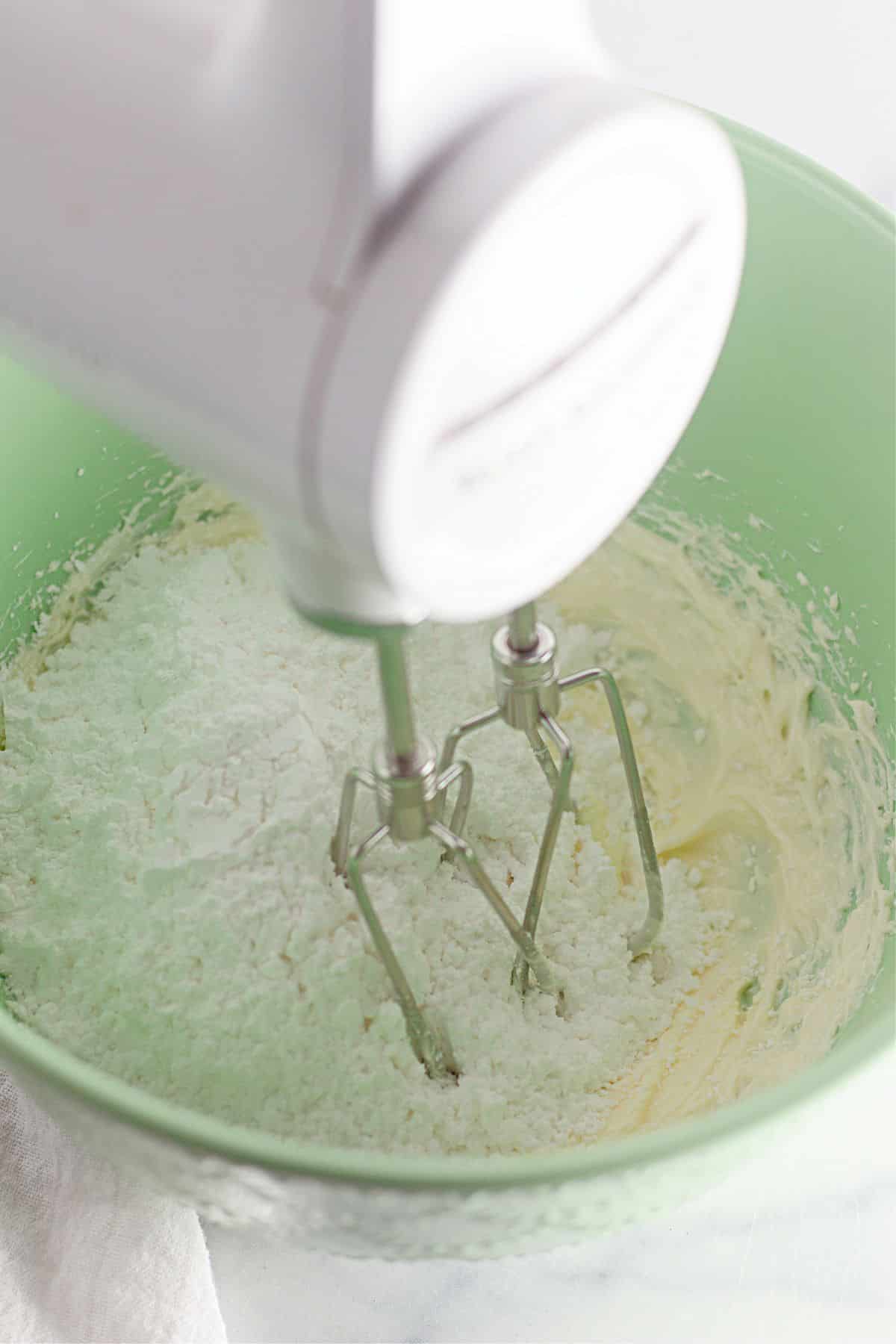 dry ingredients being added to cream butter and sugar in a mixing bowl.