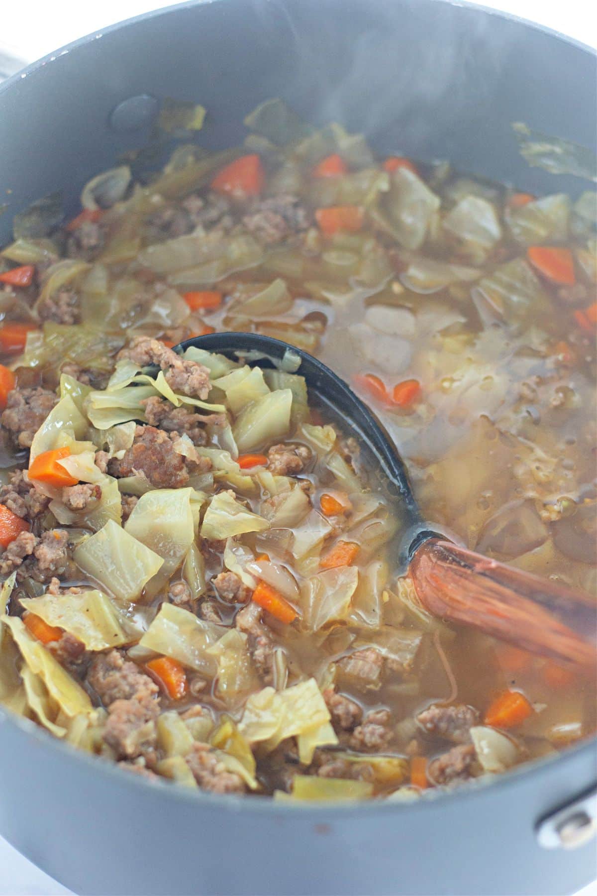 egg roll soup in a pot being stirred with a wooden spoon.
