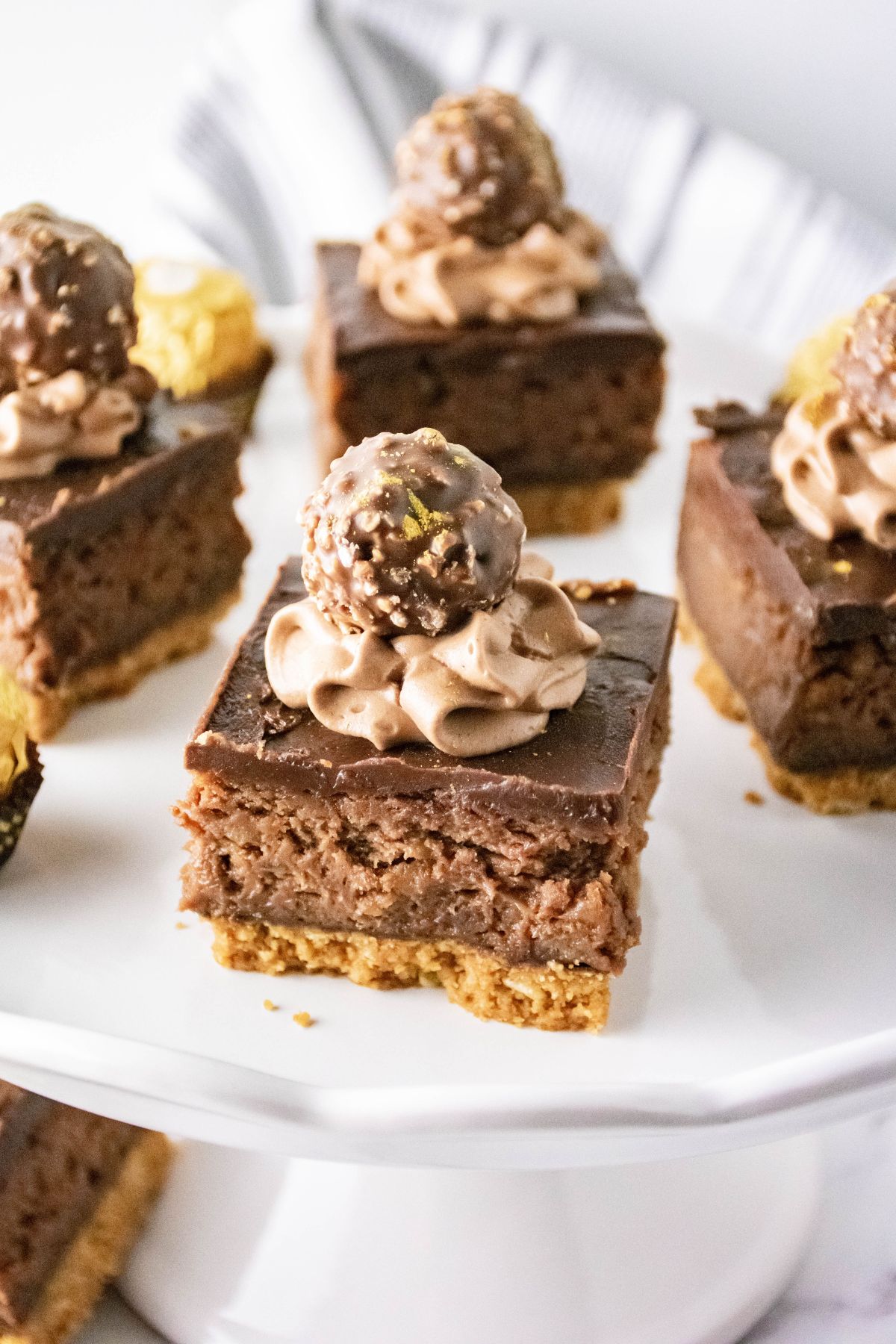 ferrero rocher cheesecake bars on a cake plate.
