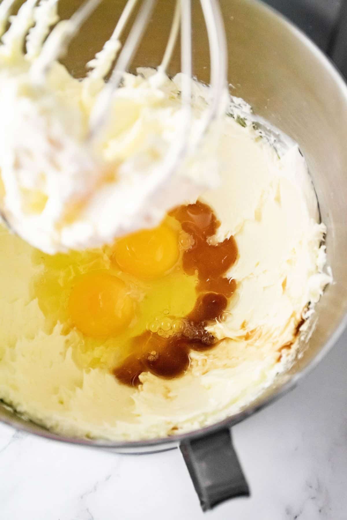 cream cheese, sugar, eggs, and vanilla extract being mixed in a stand mixer.