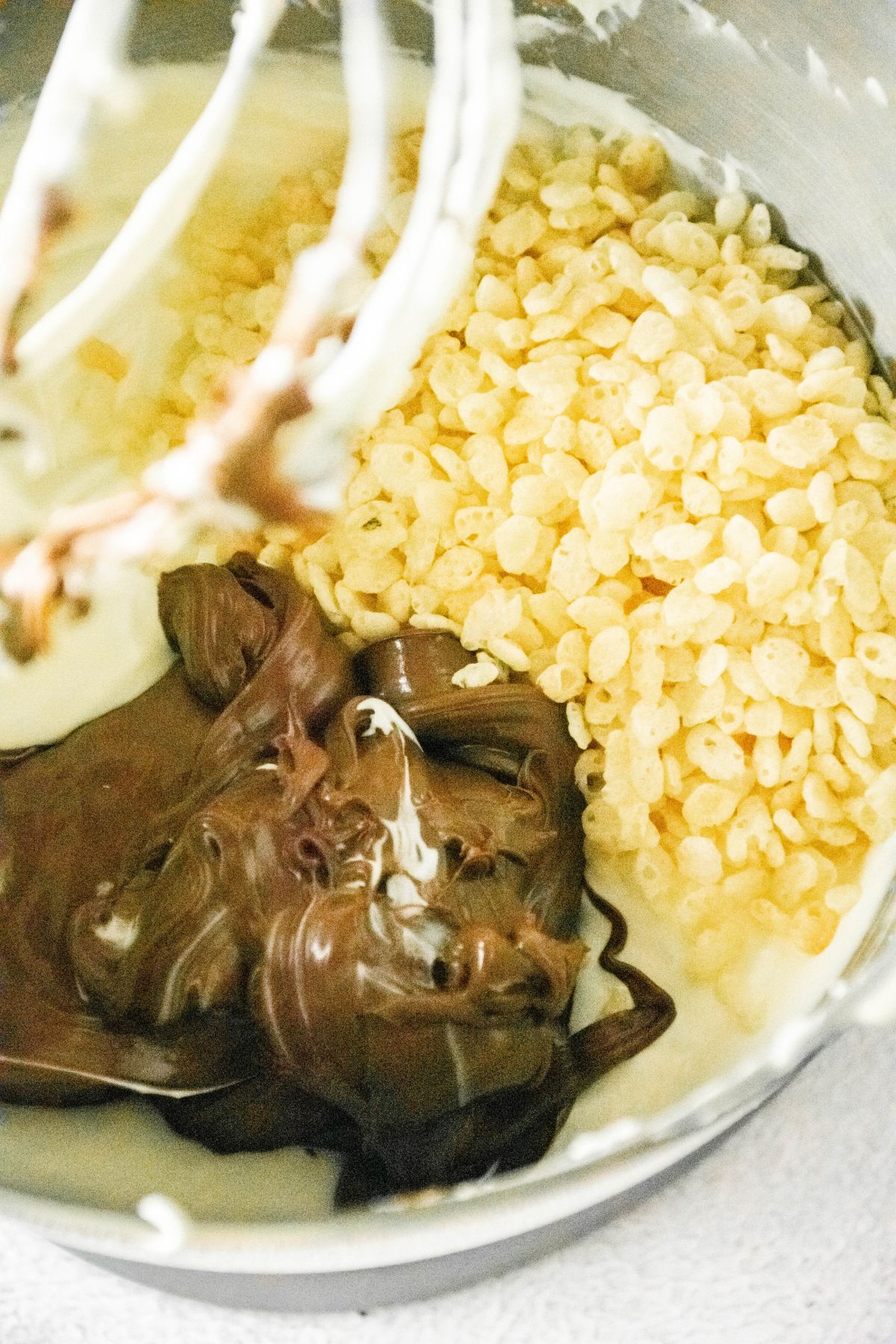 nutella and rice krispies being added to cheesecake batter in a stand mixer.