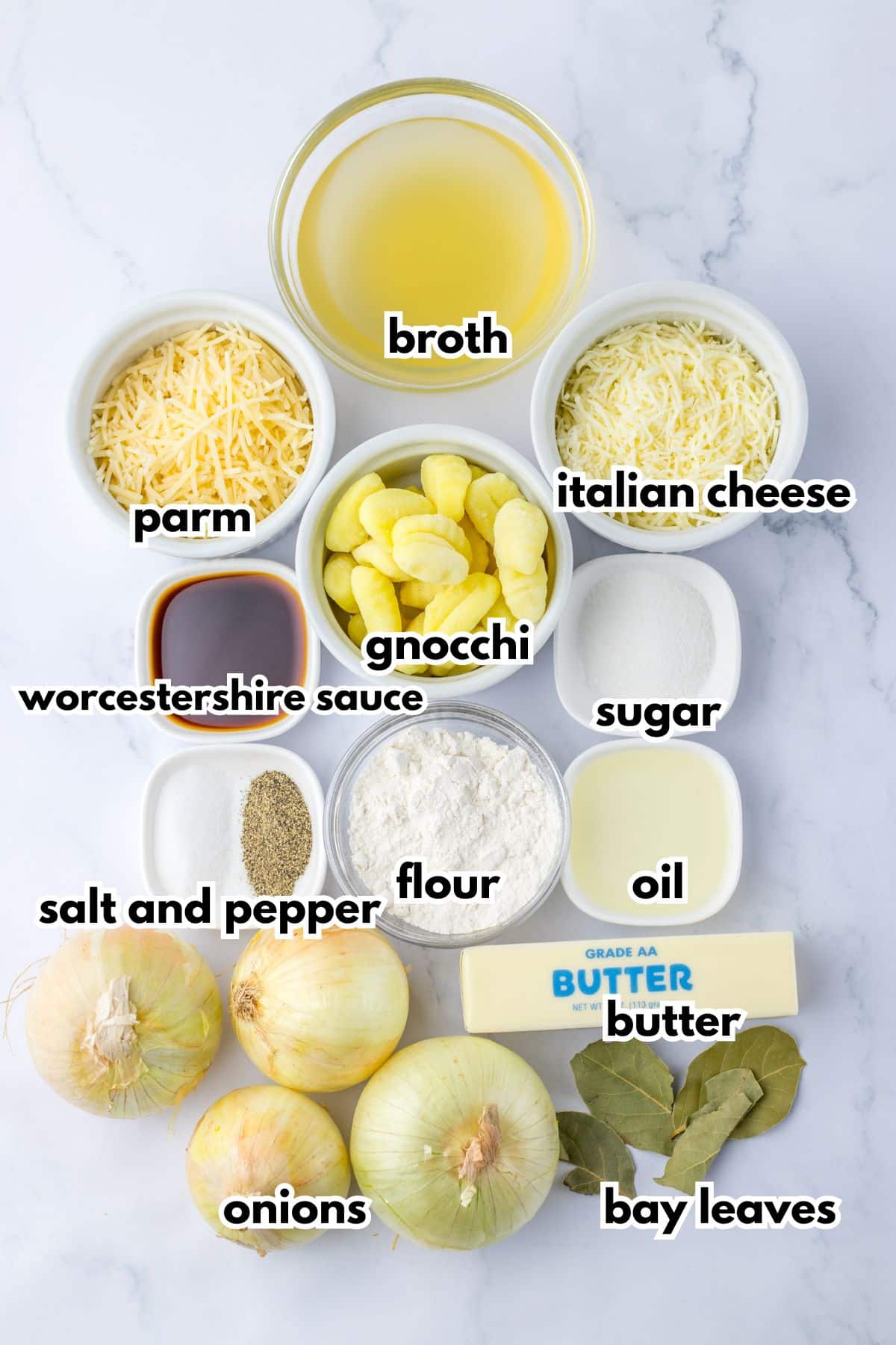 broth, parmesan, italian cheese, gnocchi, worcestershire sauce, sugar, salt and pepper, flour, oil, butter, onions and bay leaves on a counter.