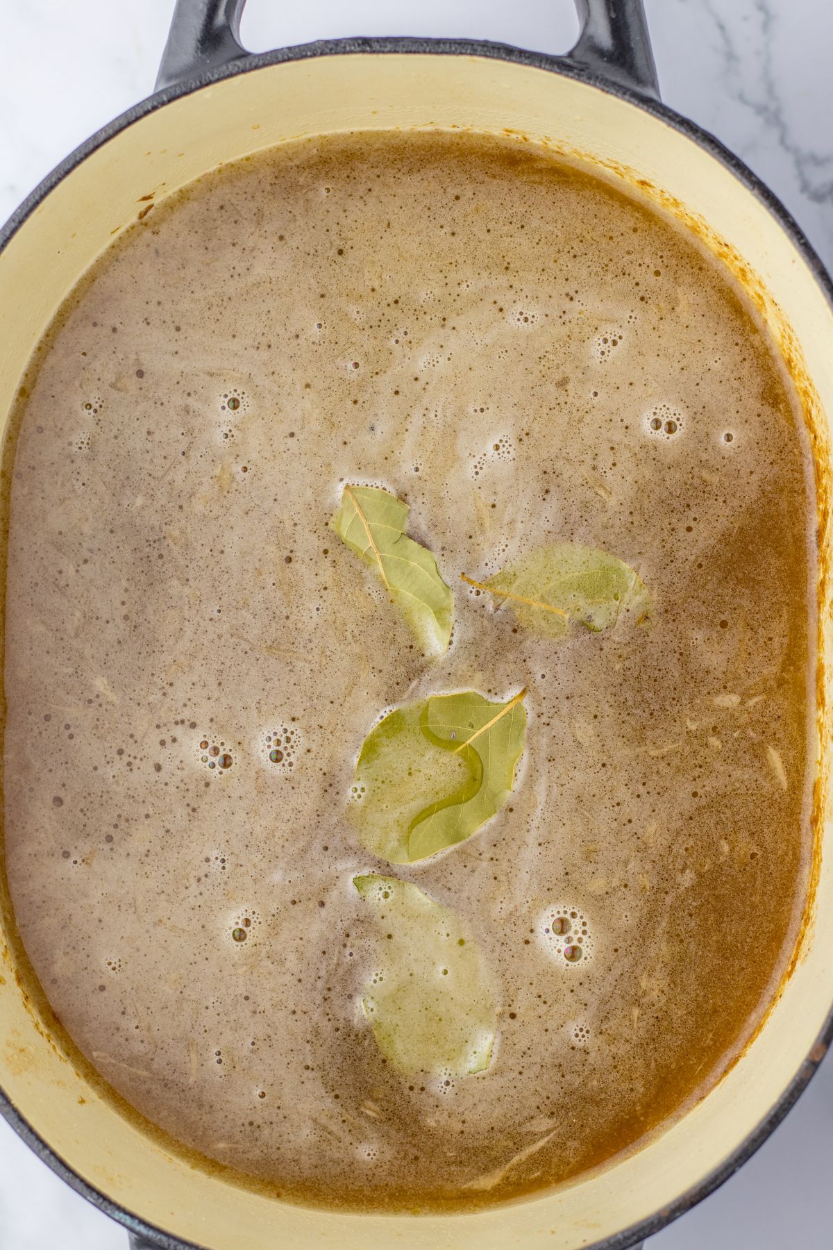 bay leaves being added to a pot of soup.