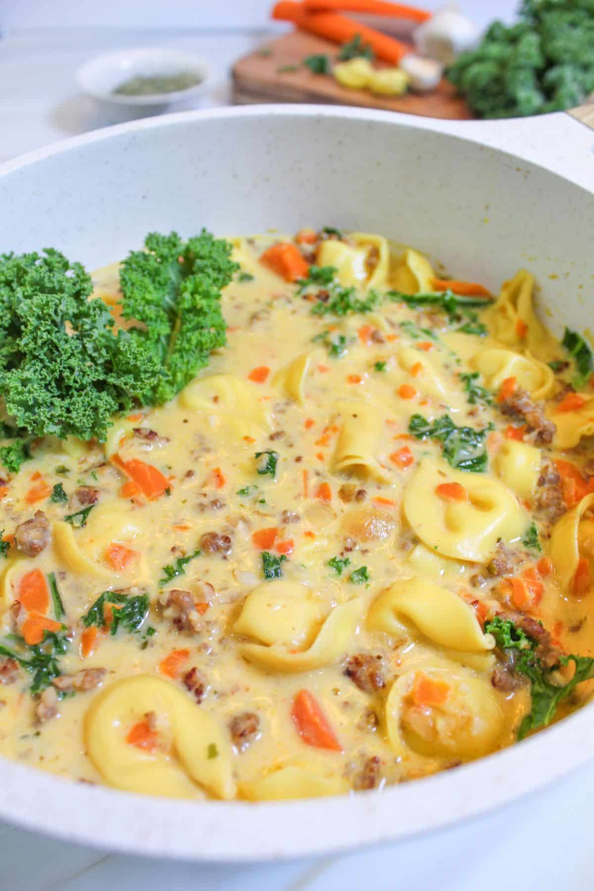 pot full of kale sausage tortellini soup garnished with kale.