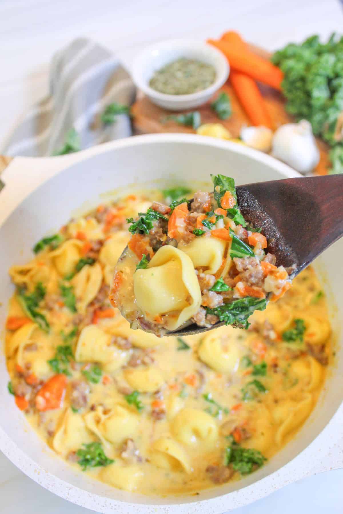 wooden spoonful of kale sausage tortellini soup held in the air.