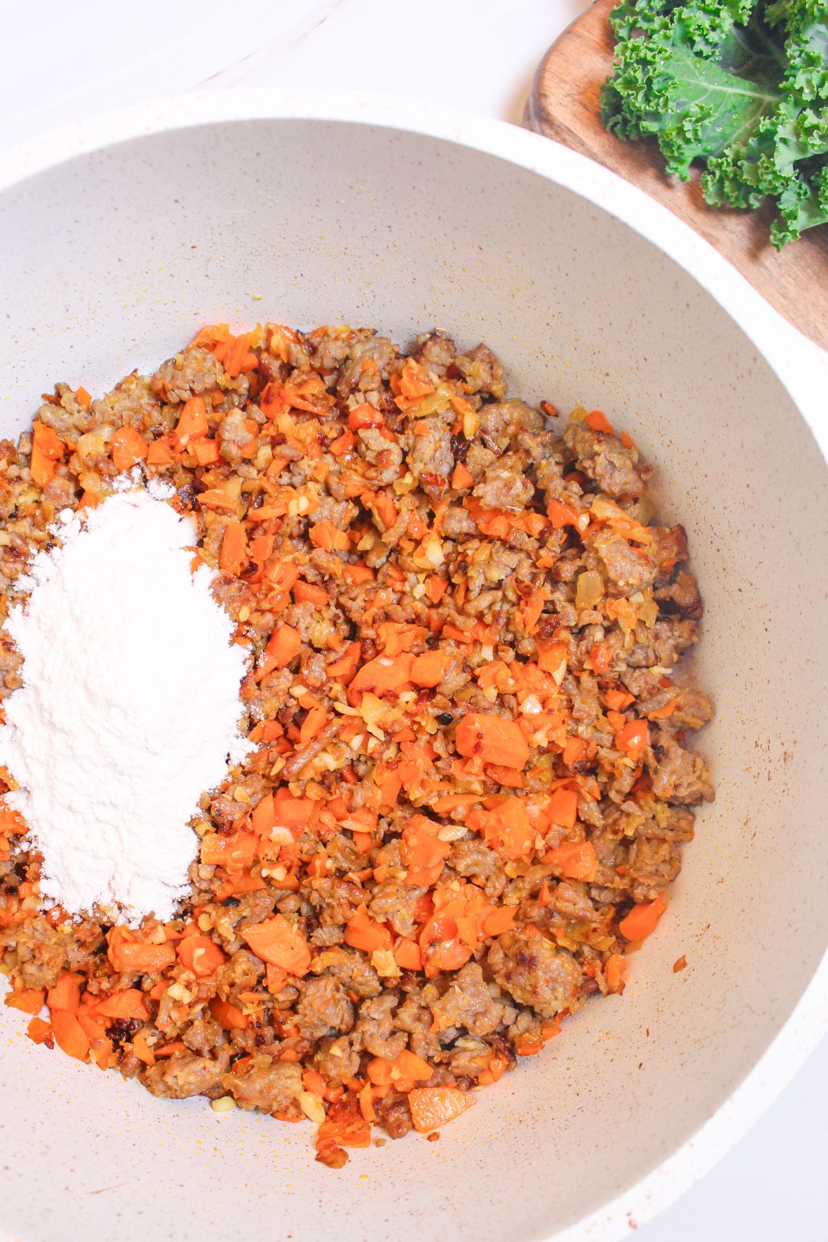 flour being added to cooked sausage, carrots, and garlic.