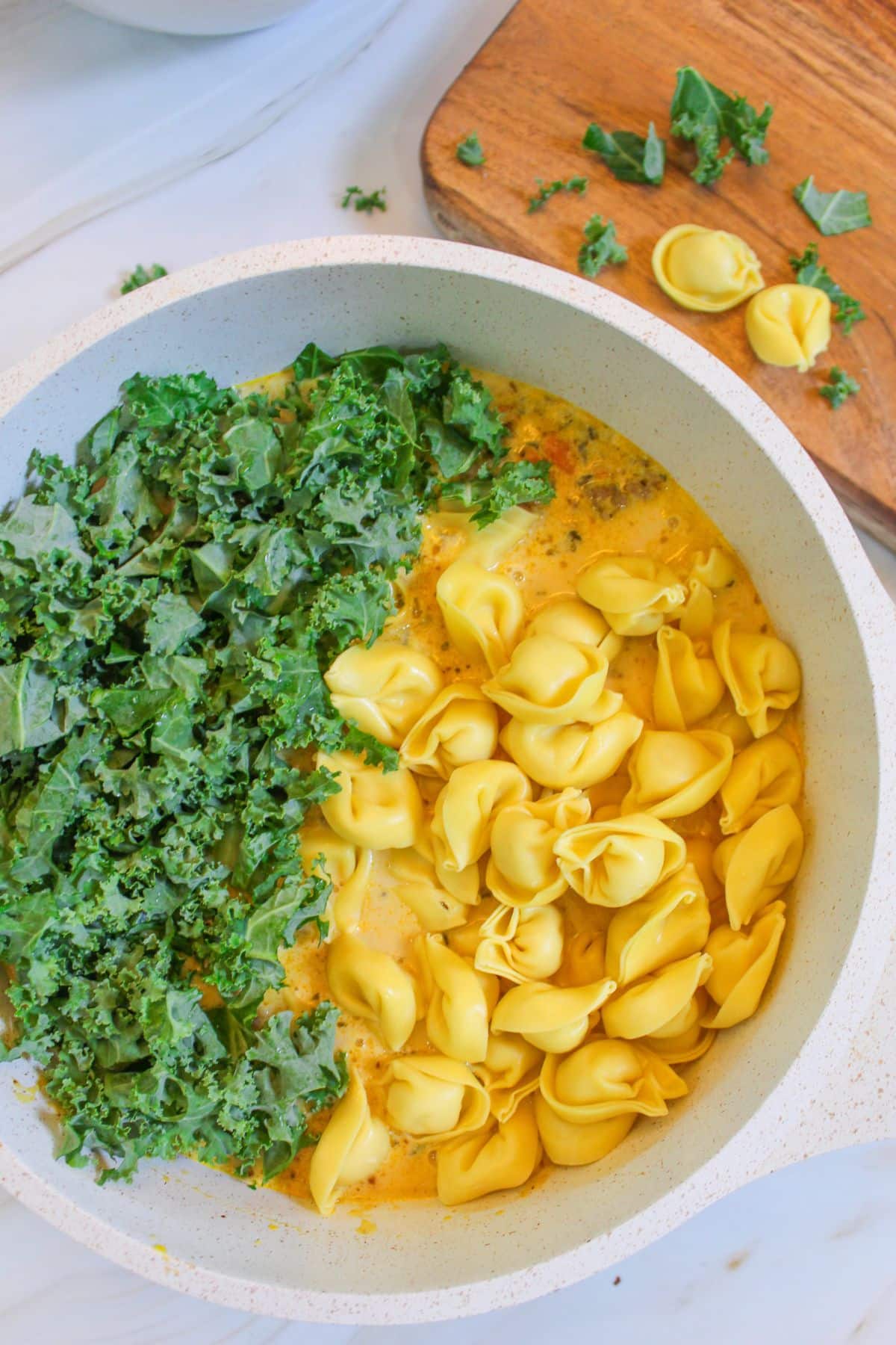 tortellini and kale being added to a pot of soup.