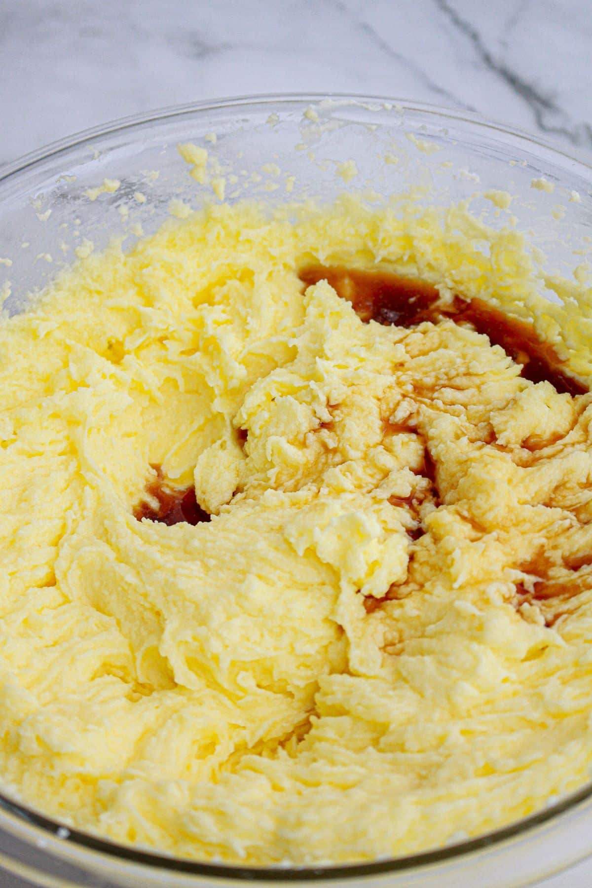 vanilla extract being added to butter and sugar in a glass mixing bowl.