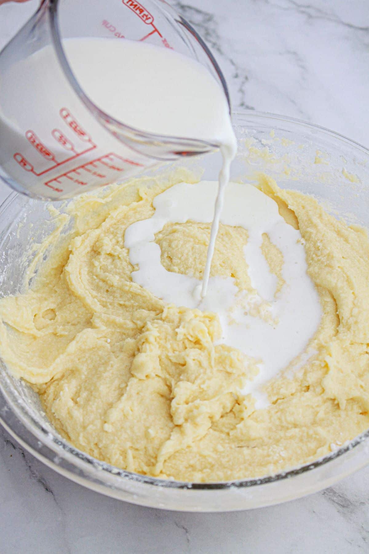 milk being added to cake batter in a glass mixing bowl.
