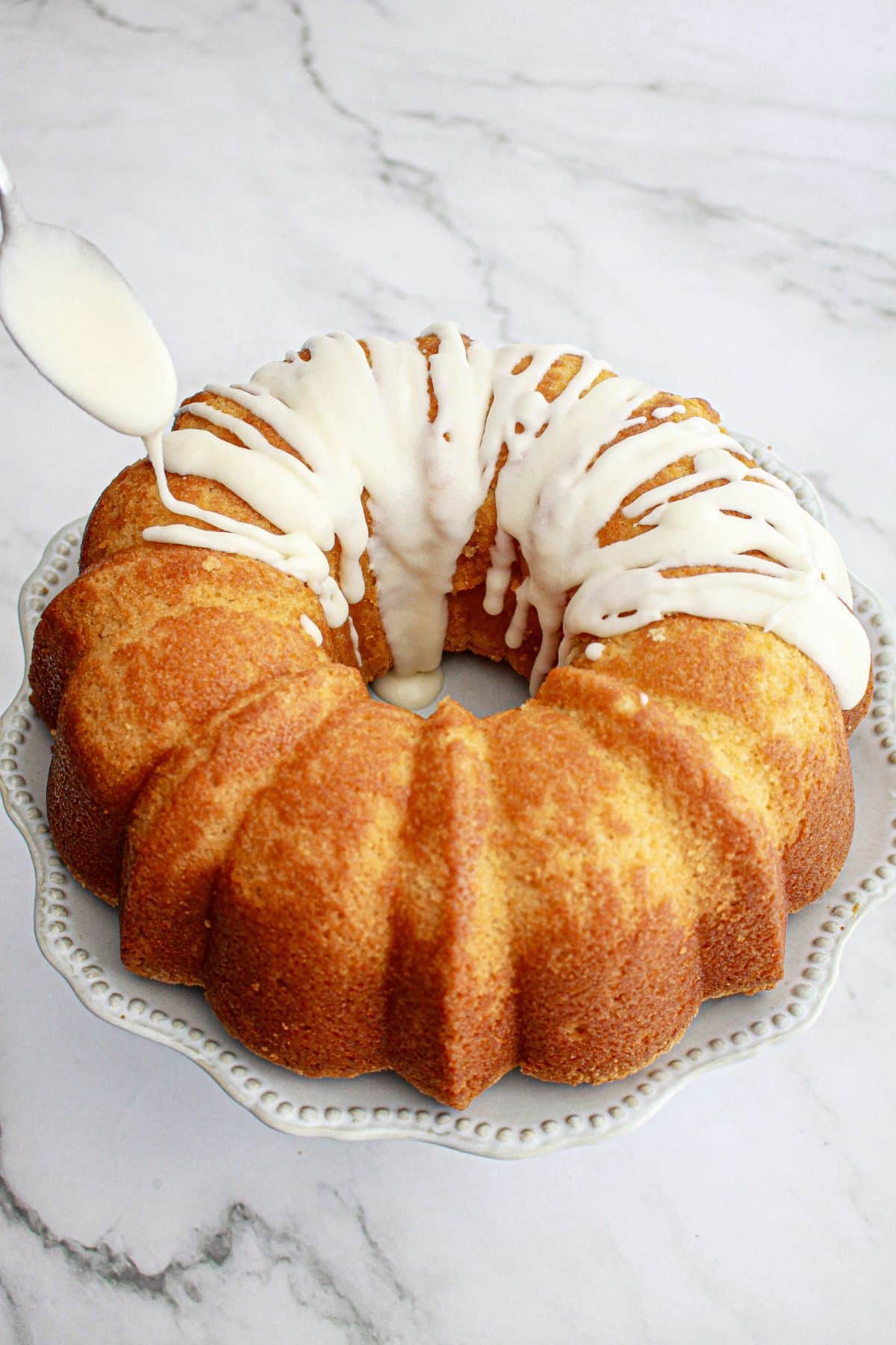 glaze being drizzled on top of a bundt cake with a spoon.
