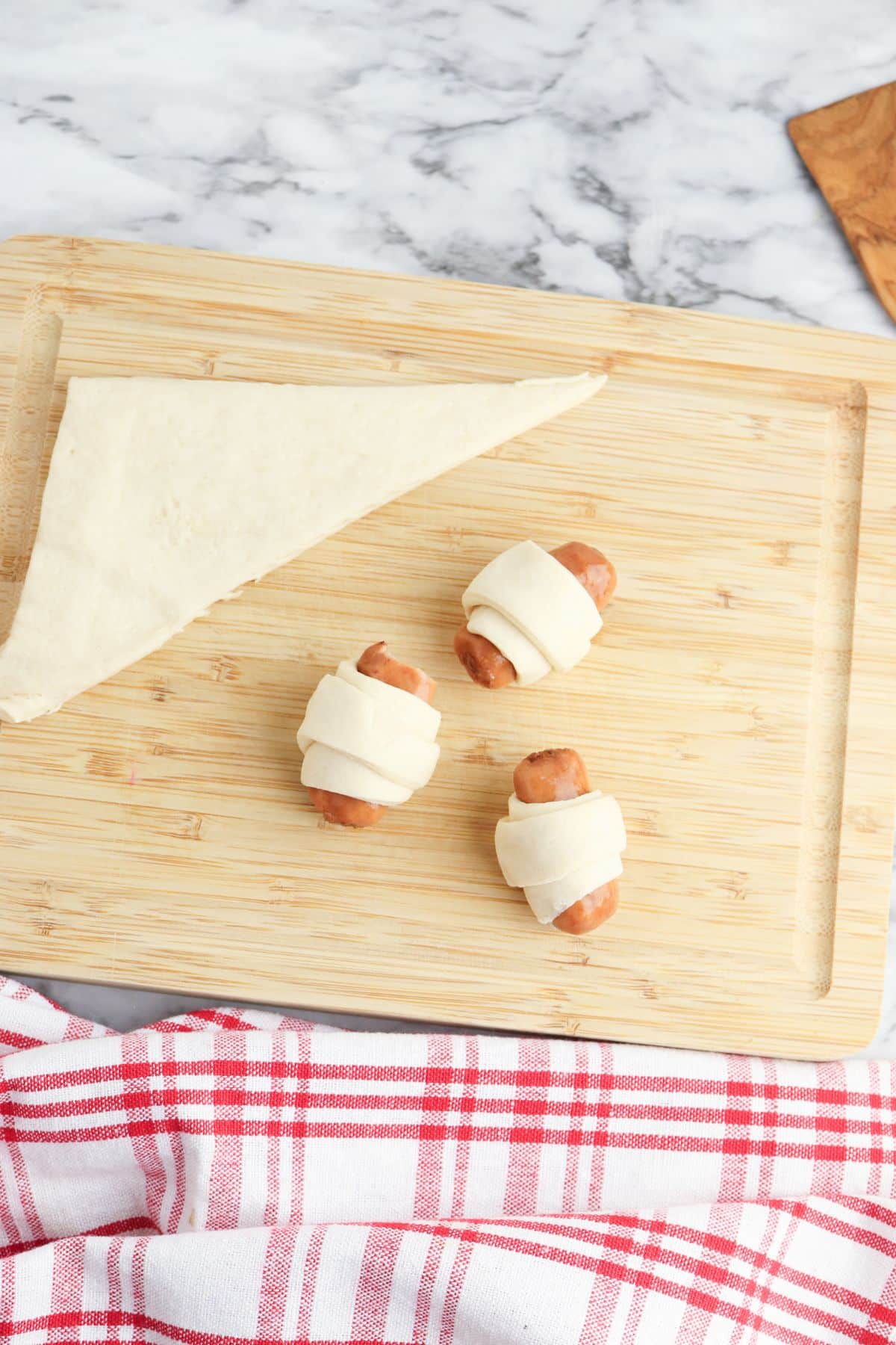 crescent rolls being wrapped around little smokies on a cutting board.