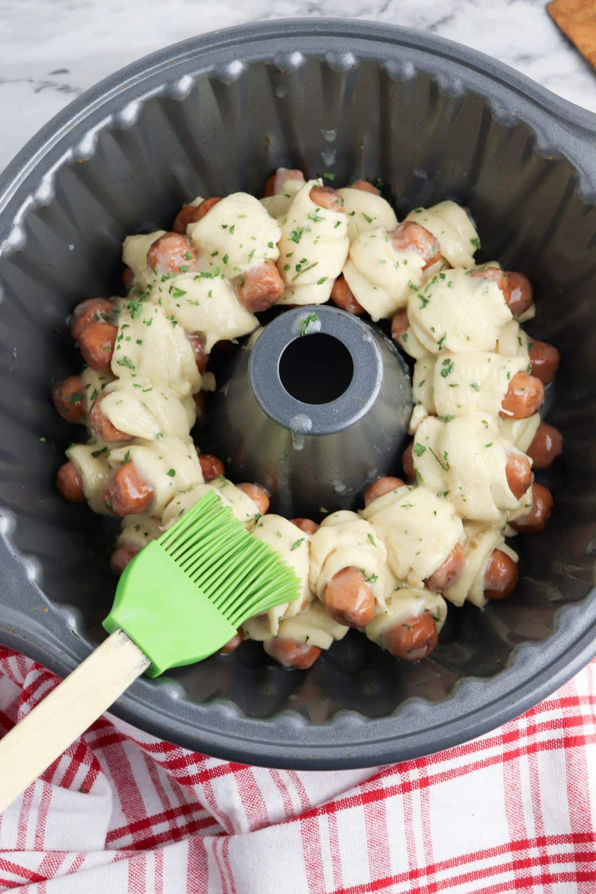 garlic butter being brushed on top of pigs in a blanket in a bundt.