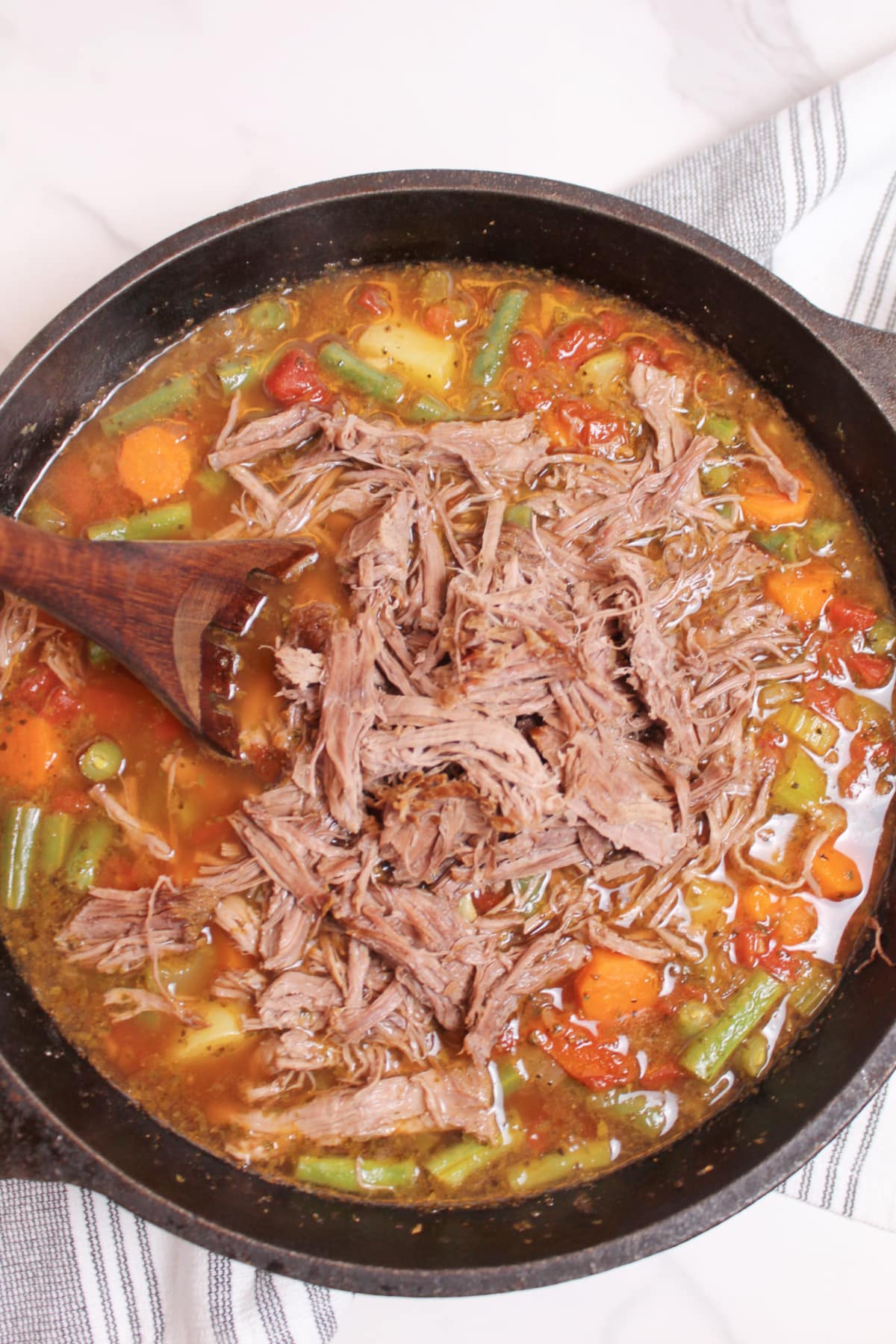 pot roast being added to a cast iron pot of vegetable soup.