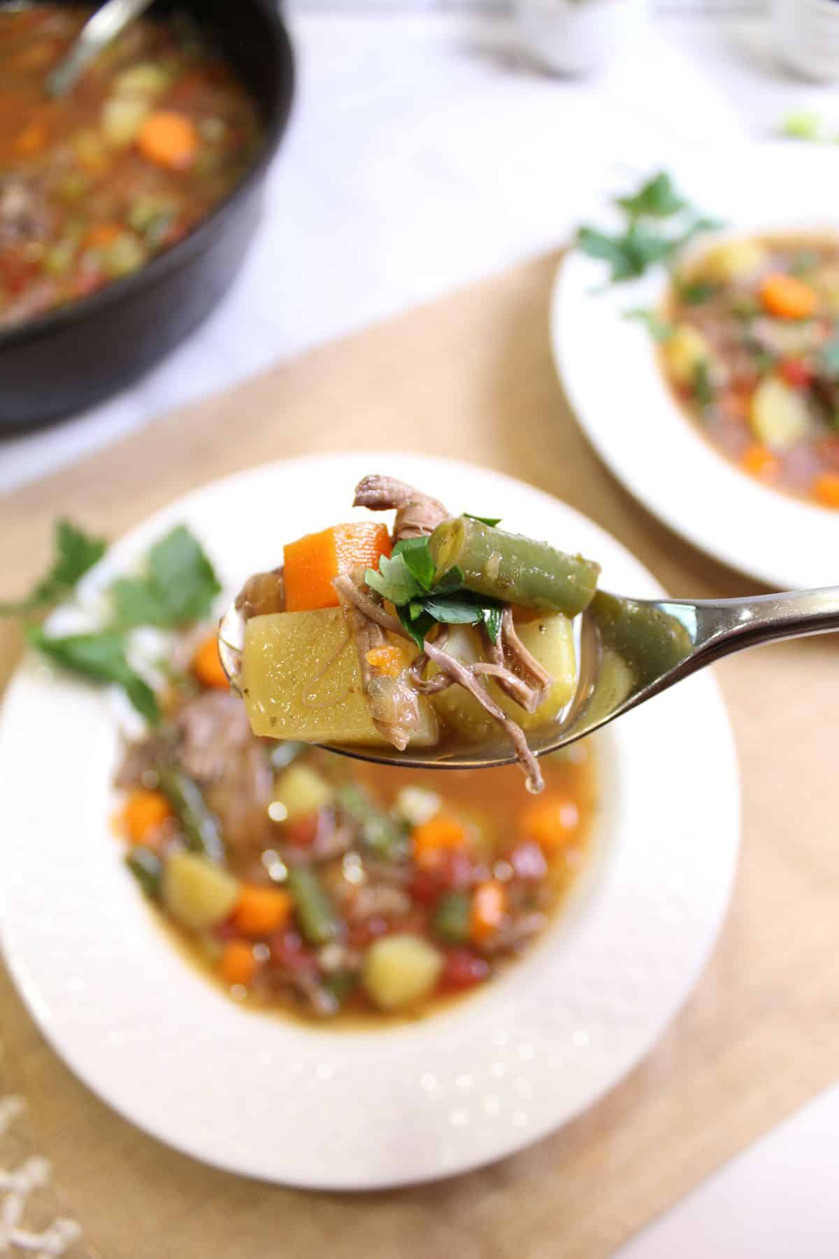 spoonful of pot roast vegetable soup held in the air above the bowl soup.