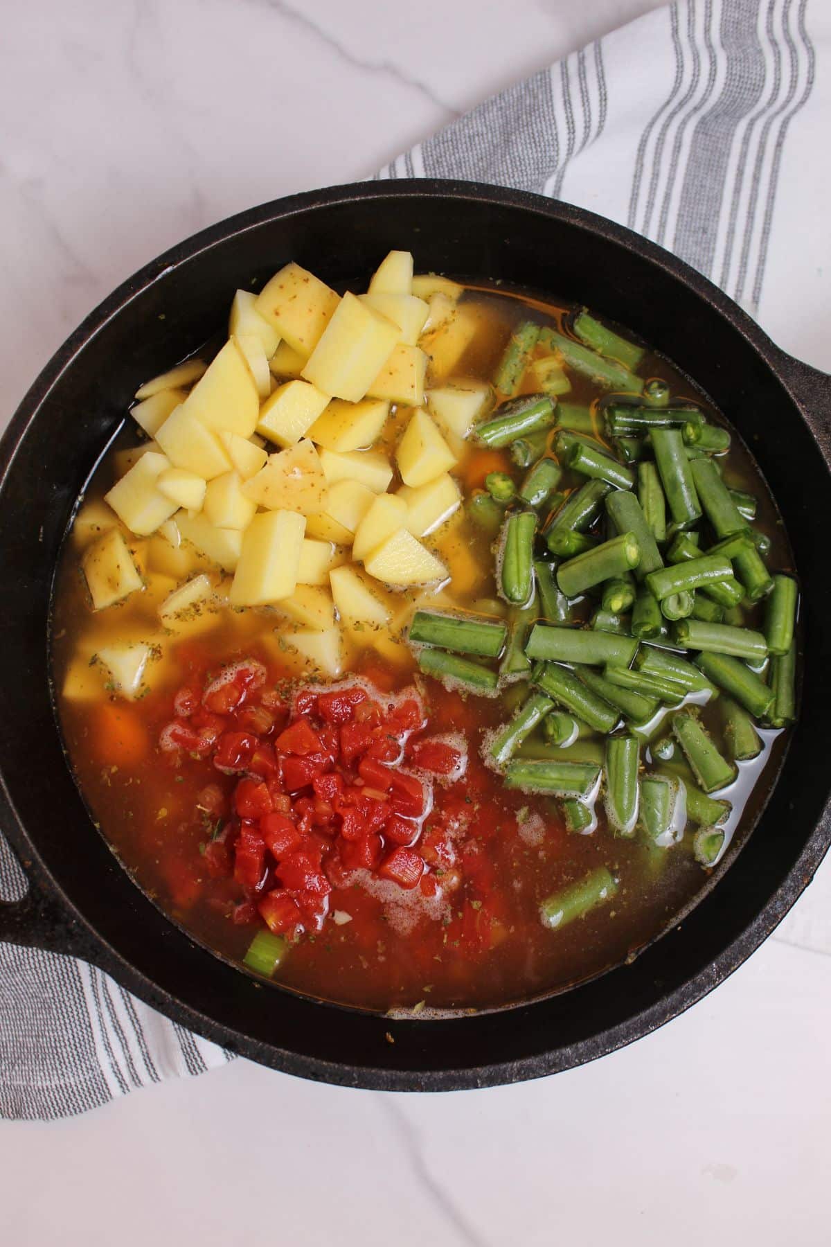potatoes, green beans, and tomatoes being added to cast iron pan.