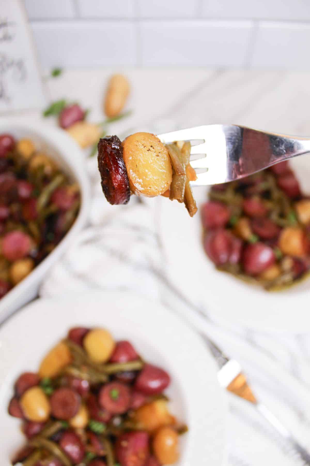 bite of potatoes and smoked sausage held in the air on a fork.