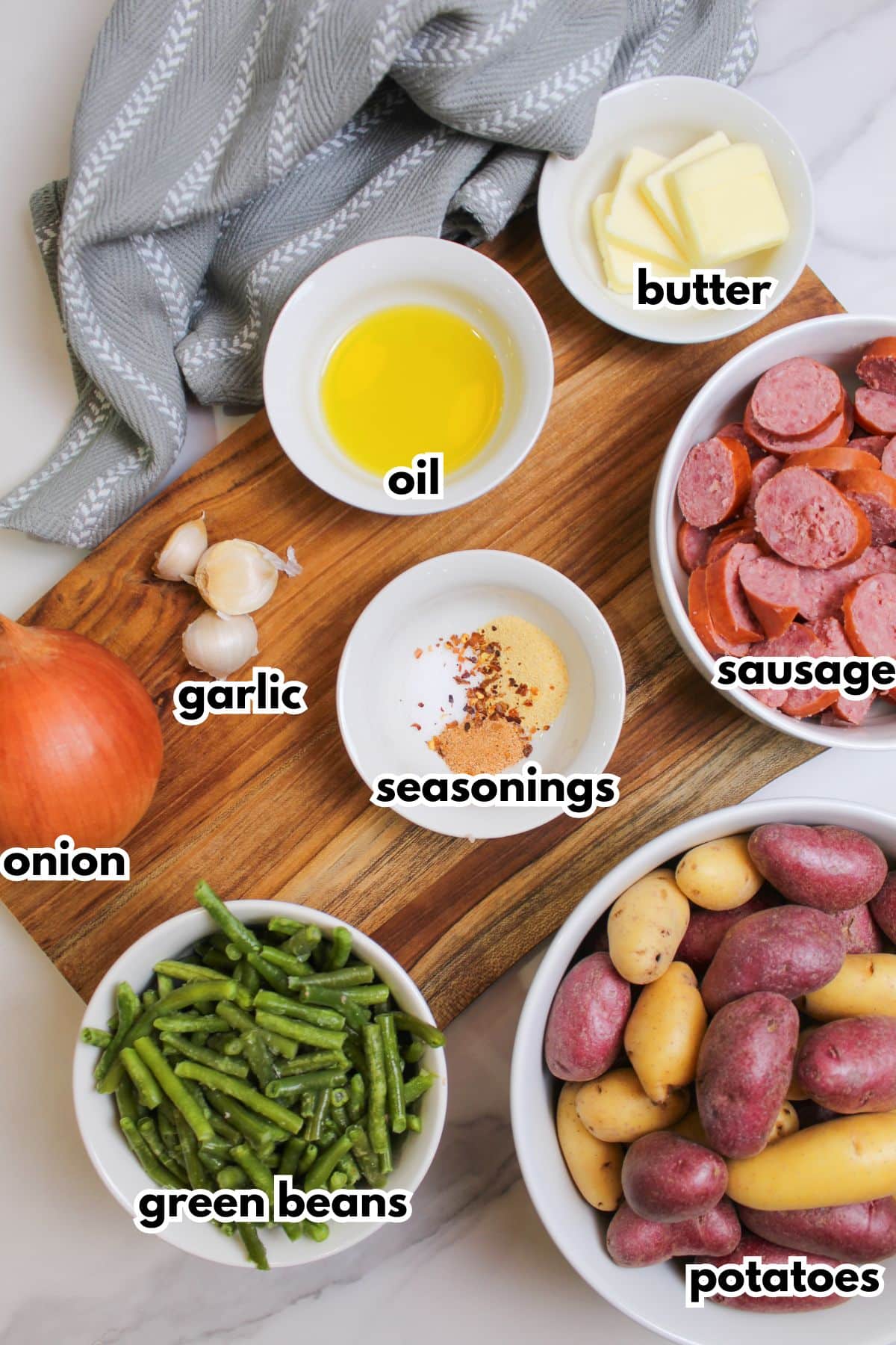 oil, butter, garlic, onion, green beans, seasonings, sausage and potatoes on a counter.