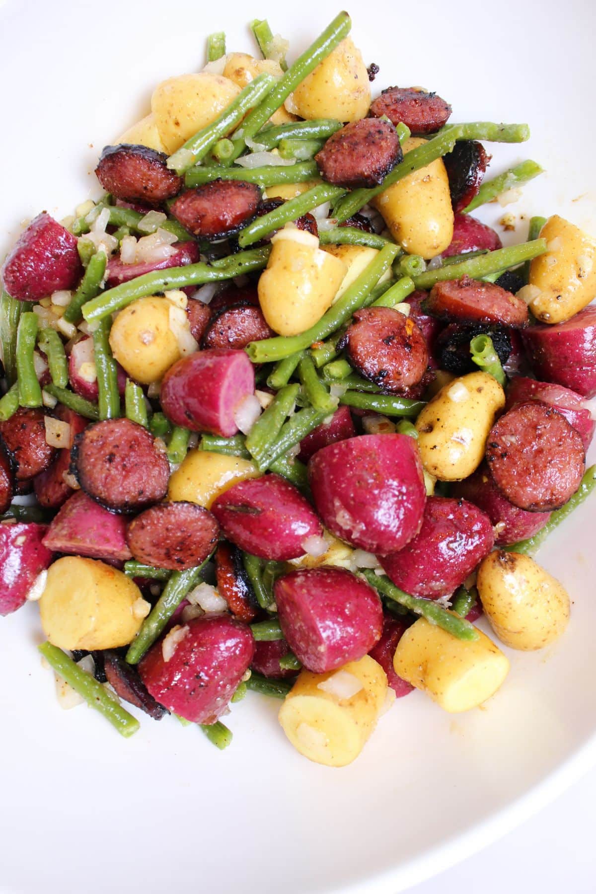 bowl full of seasoned sausage, potatoes, and green beans ready to be cooked.