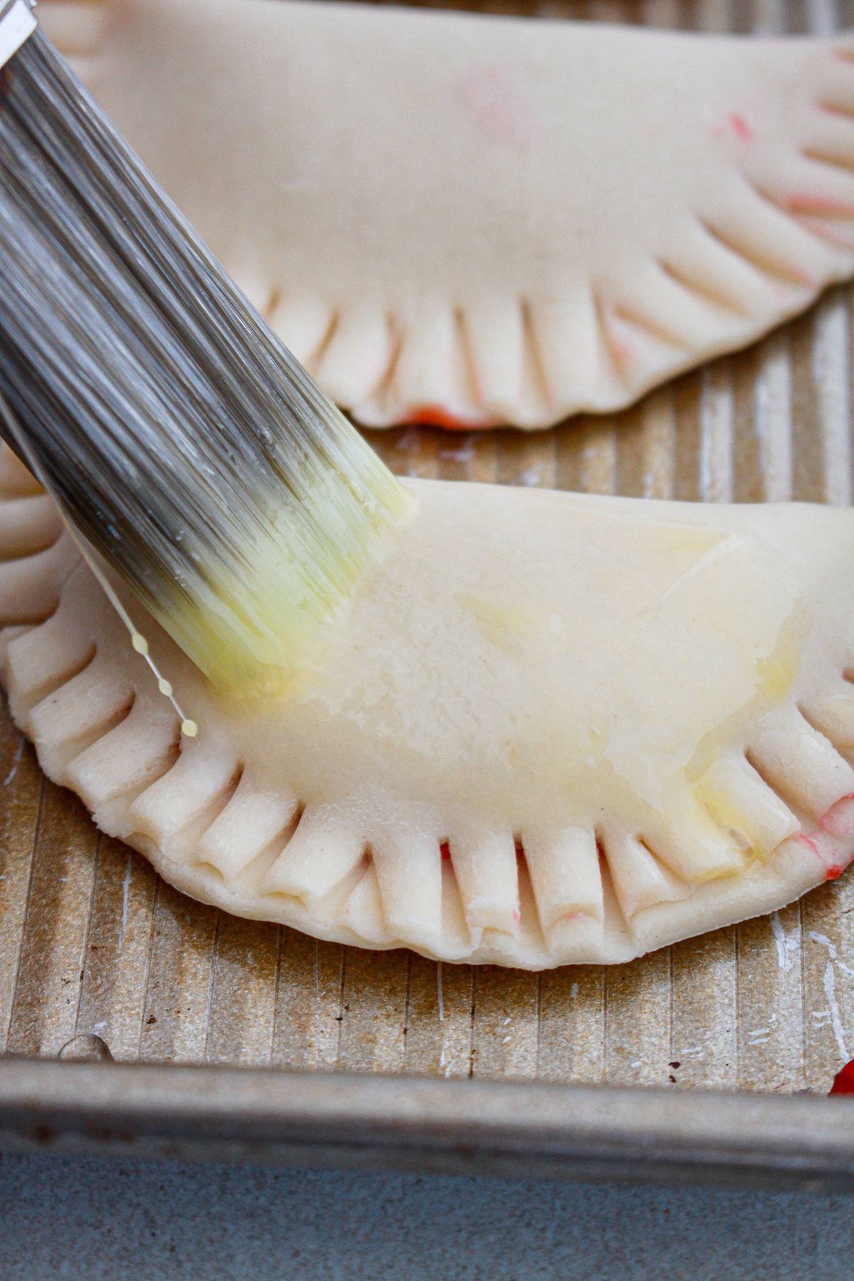 egg wash being rushed on top of raspberry hand pies.