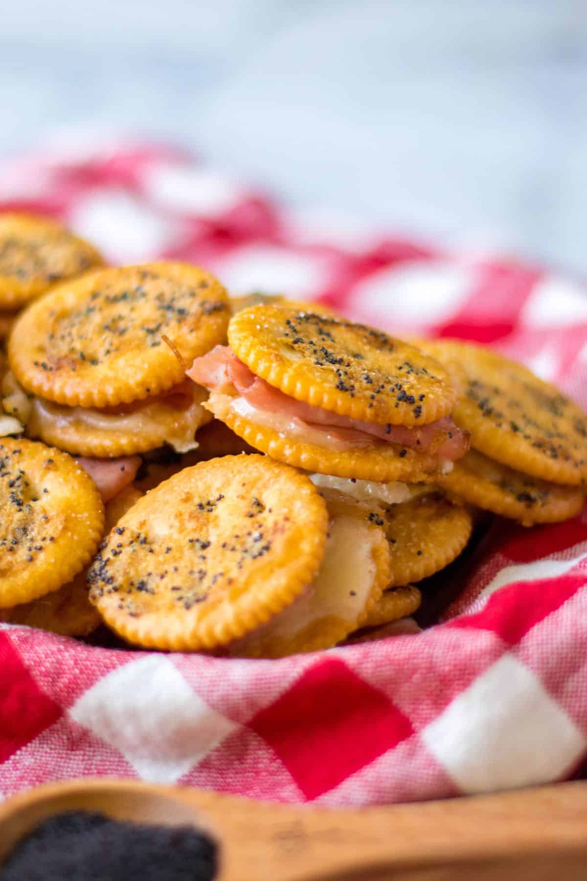 ritz ham and cheese sandwiches stacked in a basket lined with a red and white kitchen towel.