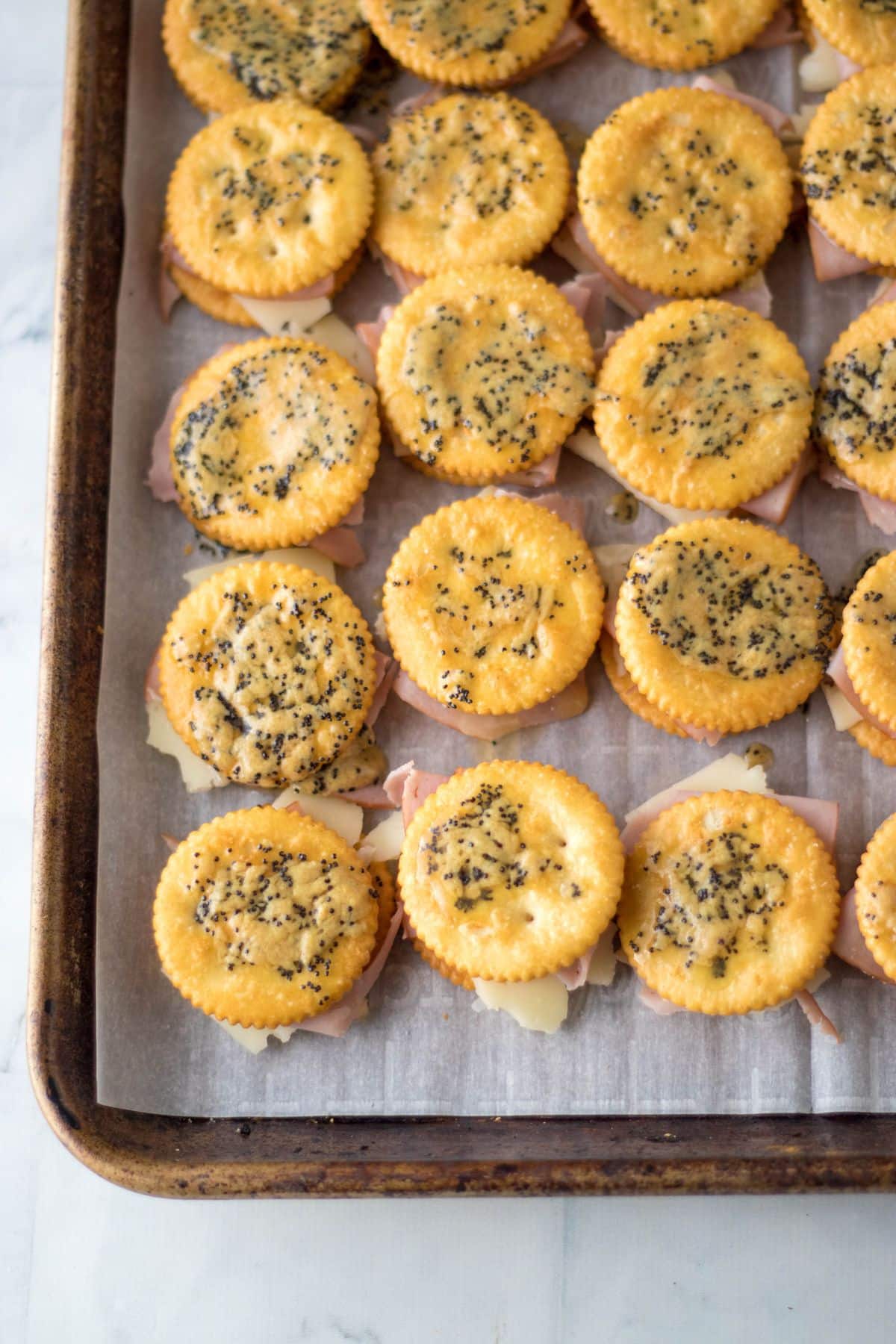 seasoning butter being brushed on top of crackers on a parchment lined baking sheet.