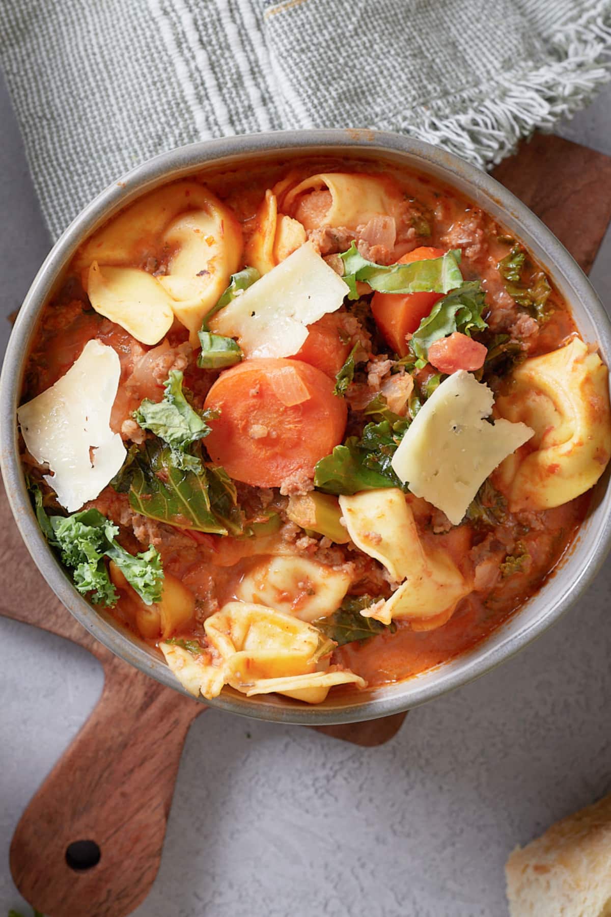 bowl full of sausage tortellini soup topped with shredded parmesan cheese.