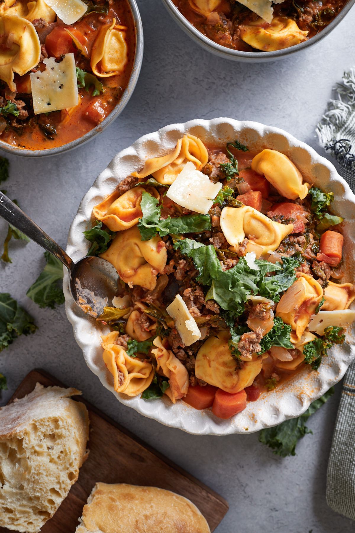 bowl full of sausage tortellini soup topped with shredded parmesan cheese.