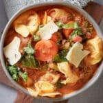 bowl full of sausage tortellini soup topped with shredded parmesan cheese.