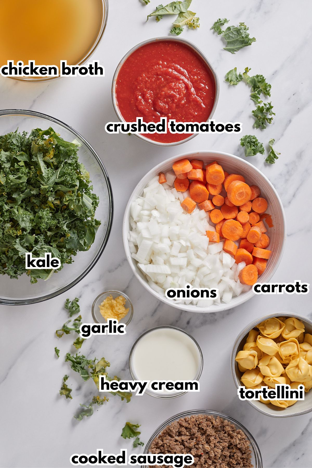 bowls of chicken broth, crushed tomatoes, kale, garlic, onions, carrots, heavy cream, tortellini, and cooked sausage.