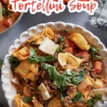 bowl full of sausage tortellini soup topped with shredded parmesan cheese.