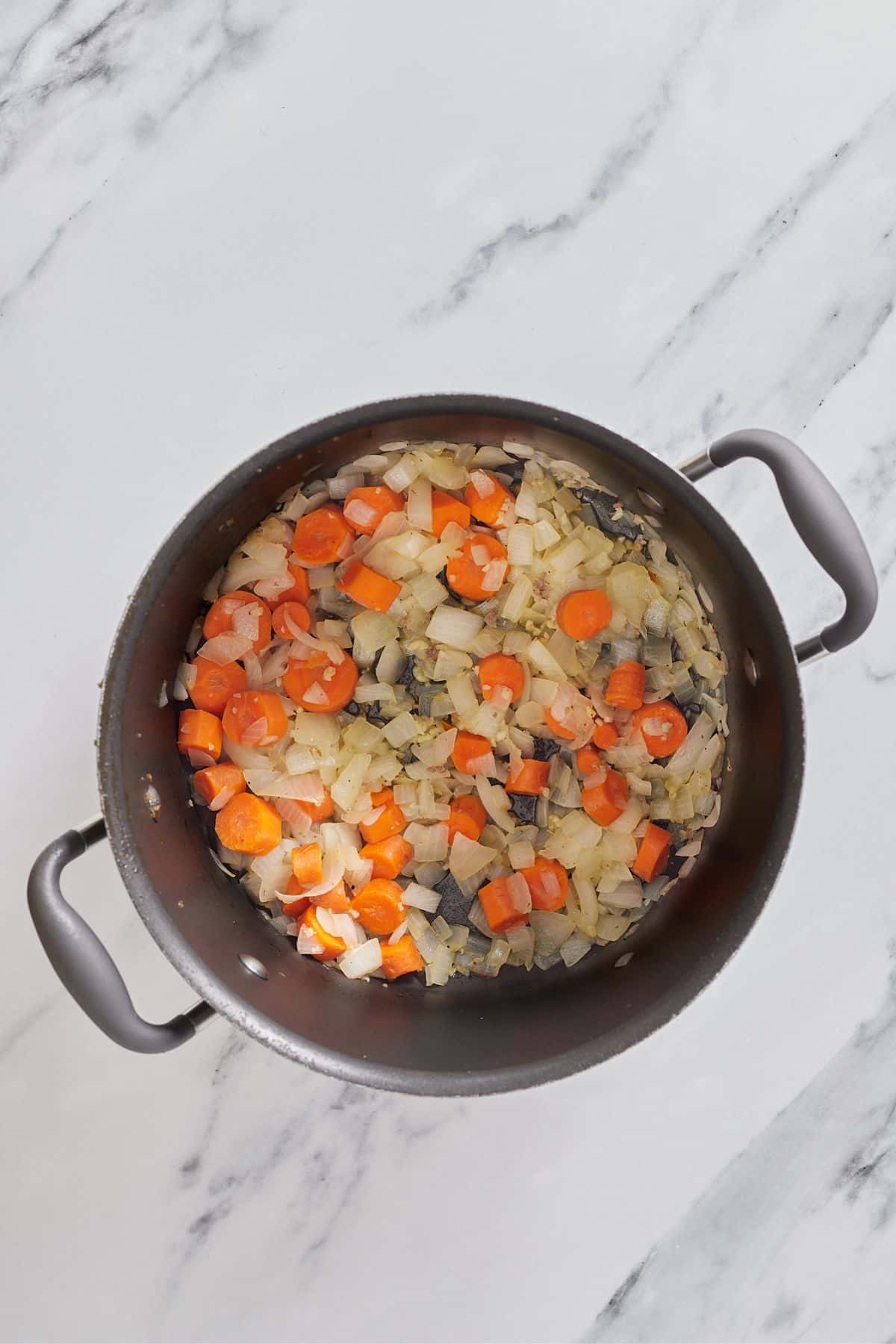 onions and carrots being sauteed in a large pot.