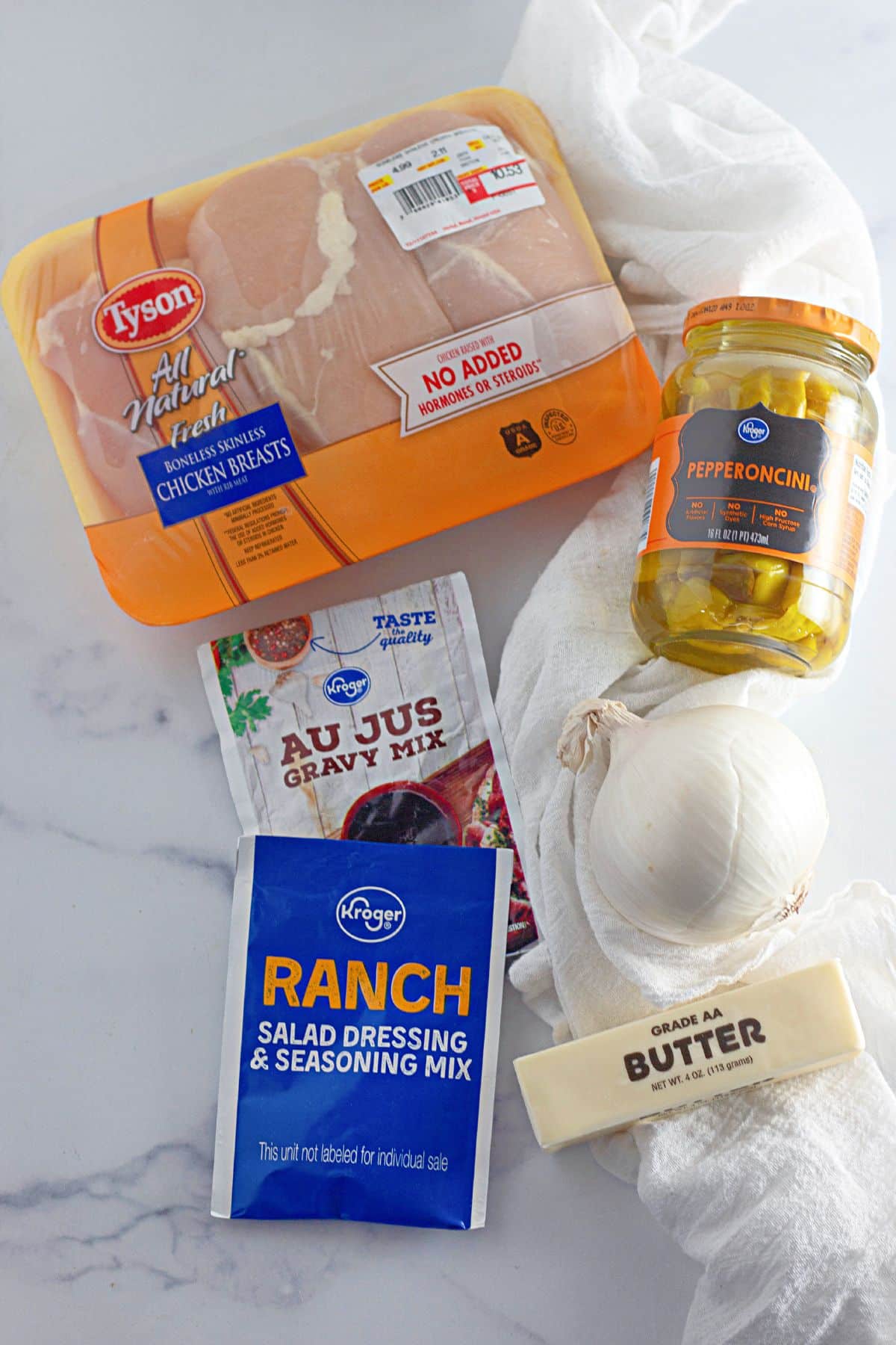 package of chicken breasts, with au just mix, ranch seasoning, a jar of pepperoncini peppers, onion, and butter.