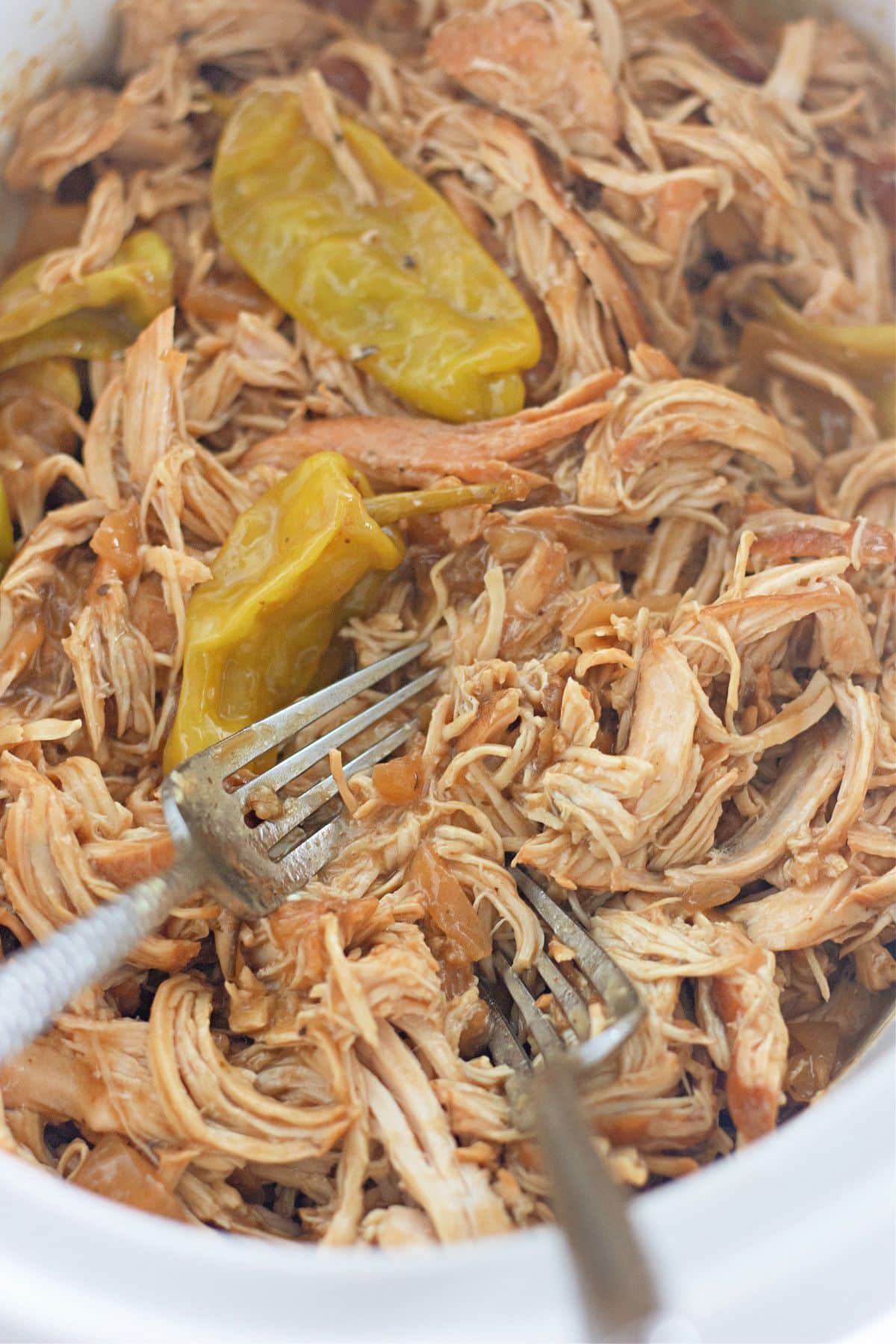 chicken being shredded in a slow cooker with two fork.