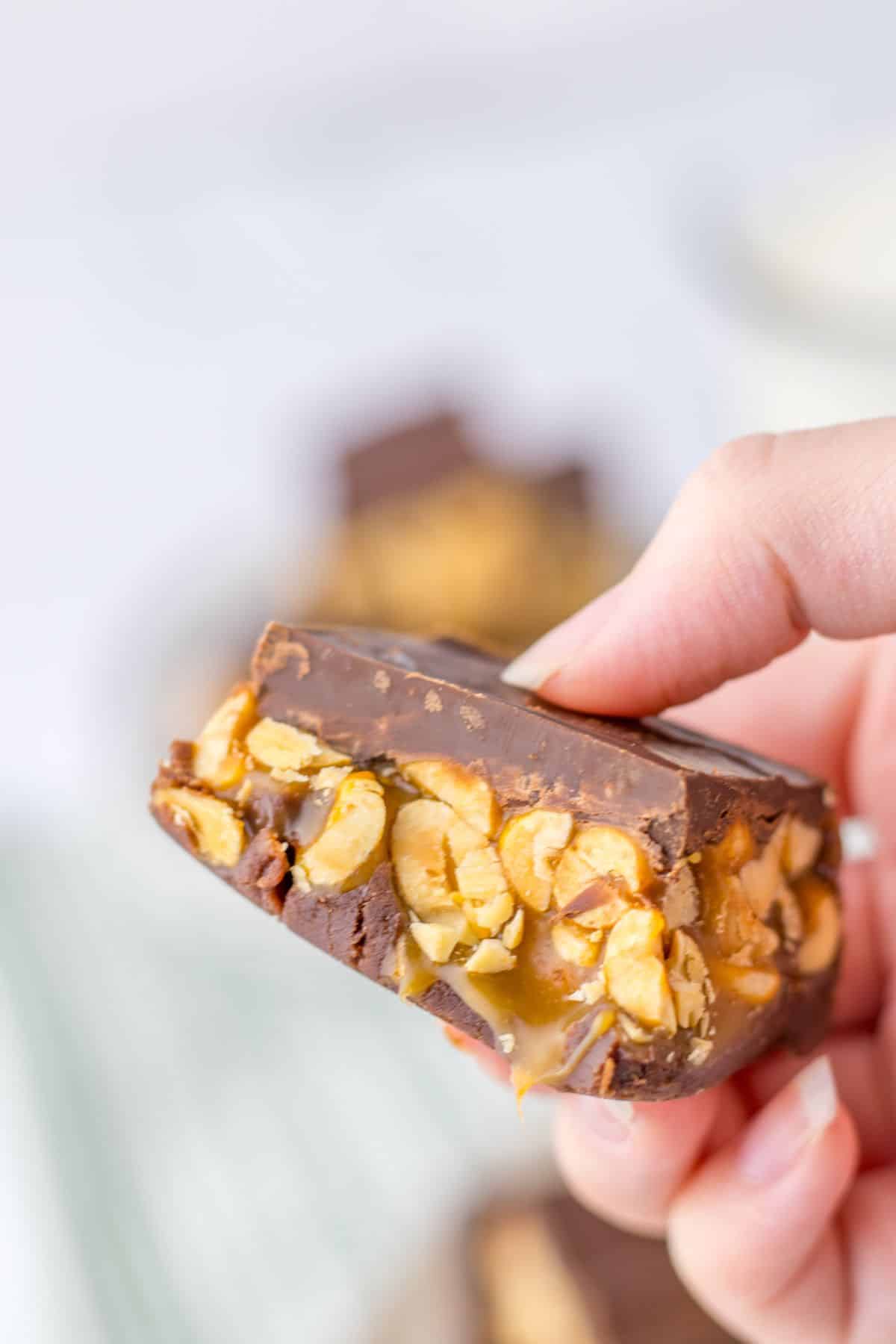 piece of snickers fudge held in a woman's hand in the air.