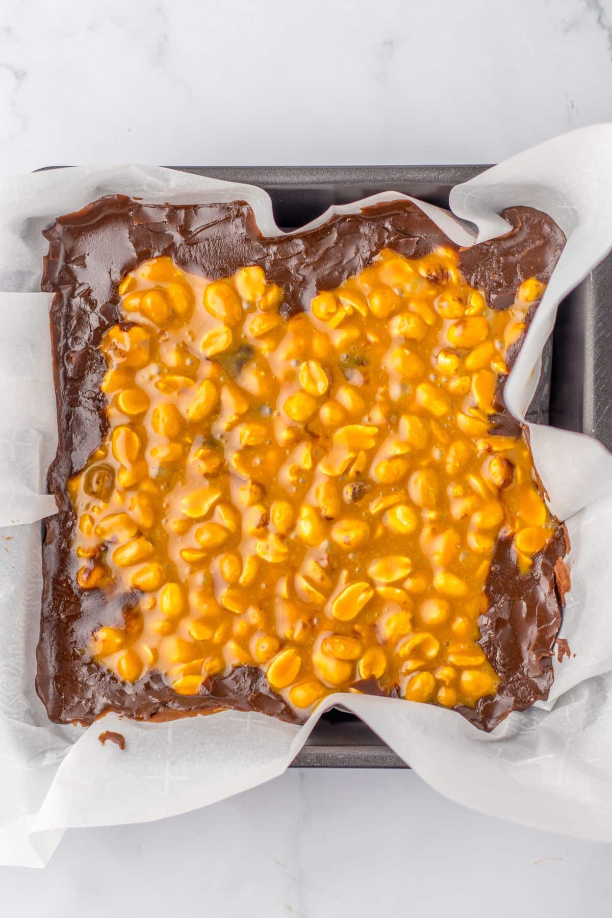 peanut layer being poured on top of the chocolate layer in a parchment lined baking sheet.