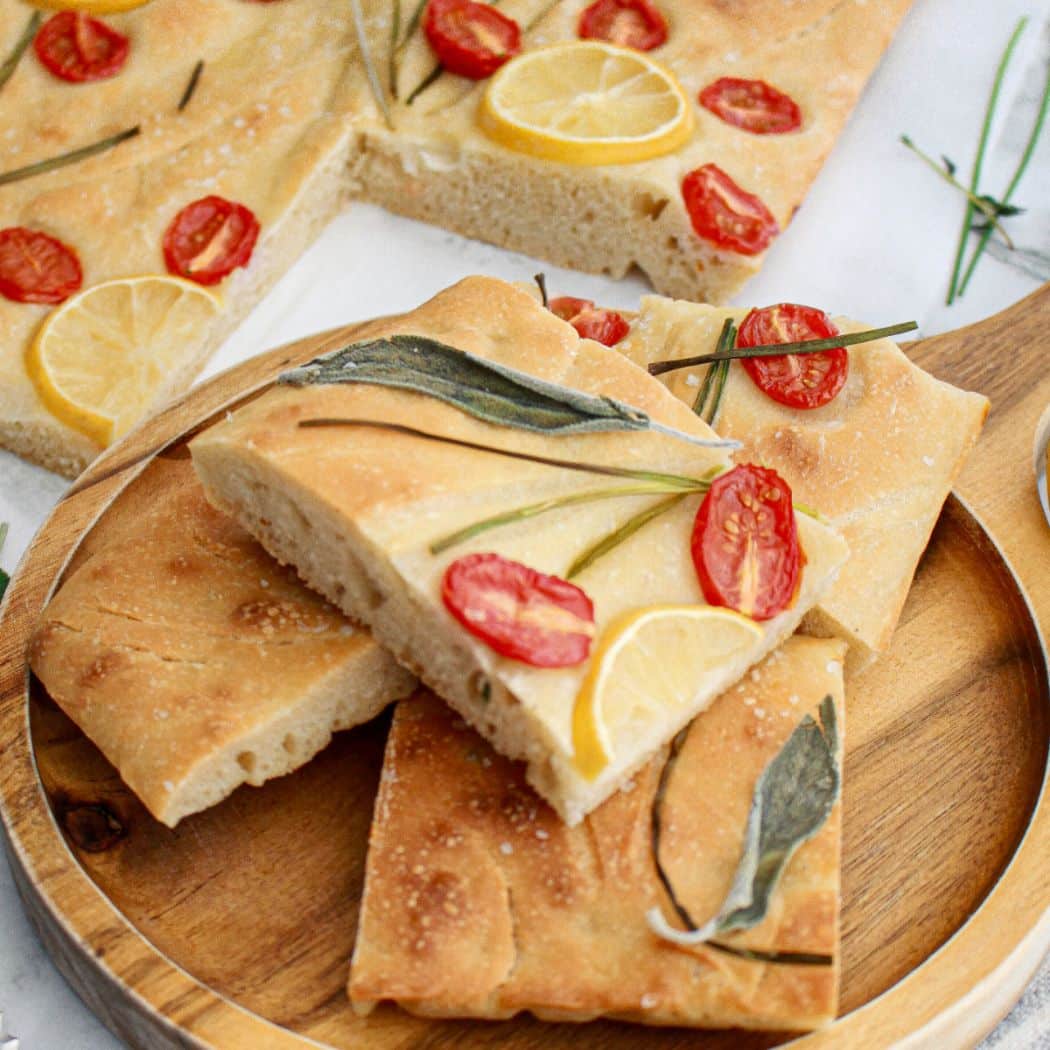 four pieces of tomato focaccia bread stacked on a wooden cutting board.