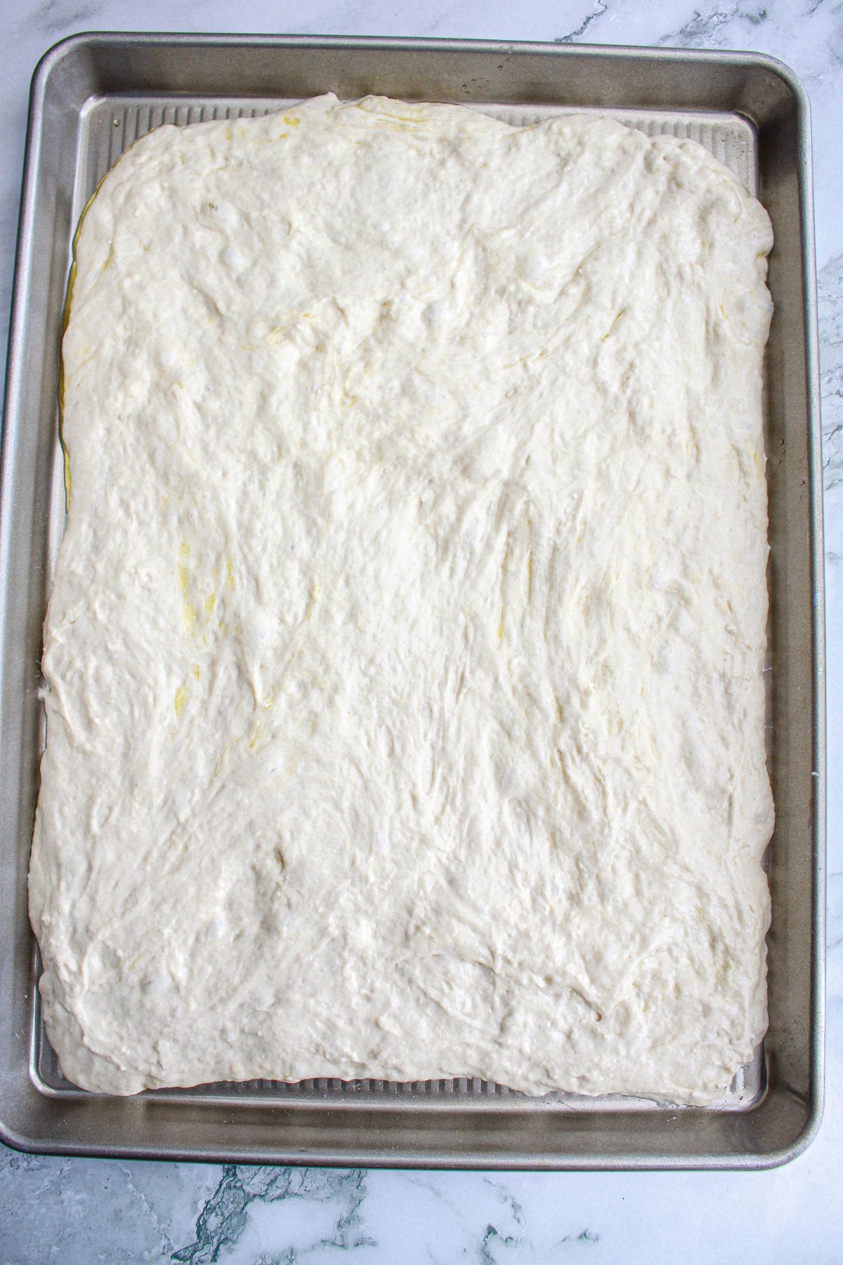 dough being pressed into a large rimmed baking sheet,