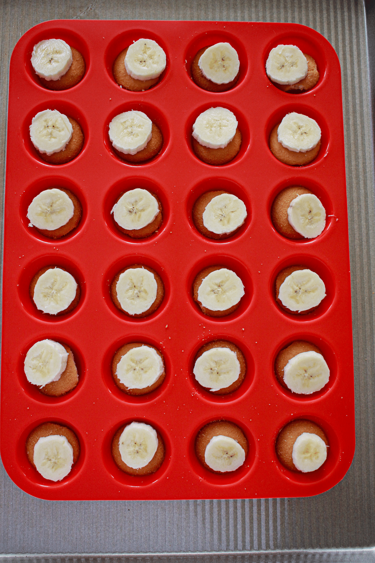 banana slice and vanilla wafer being added to a silicone muffin pan.