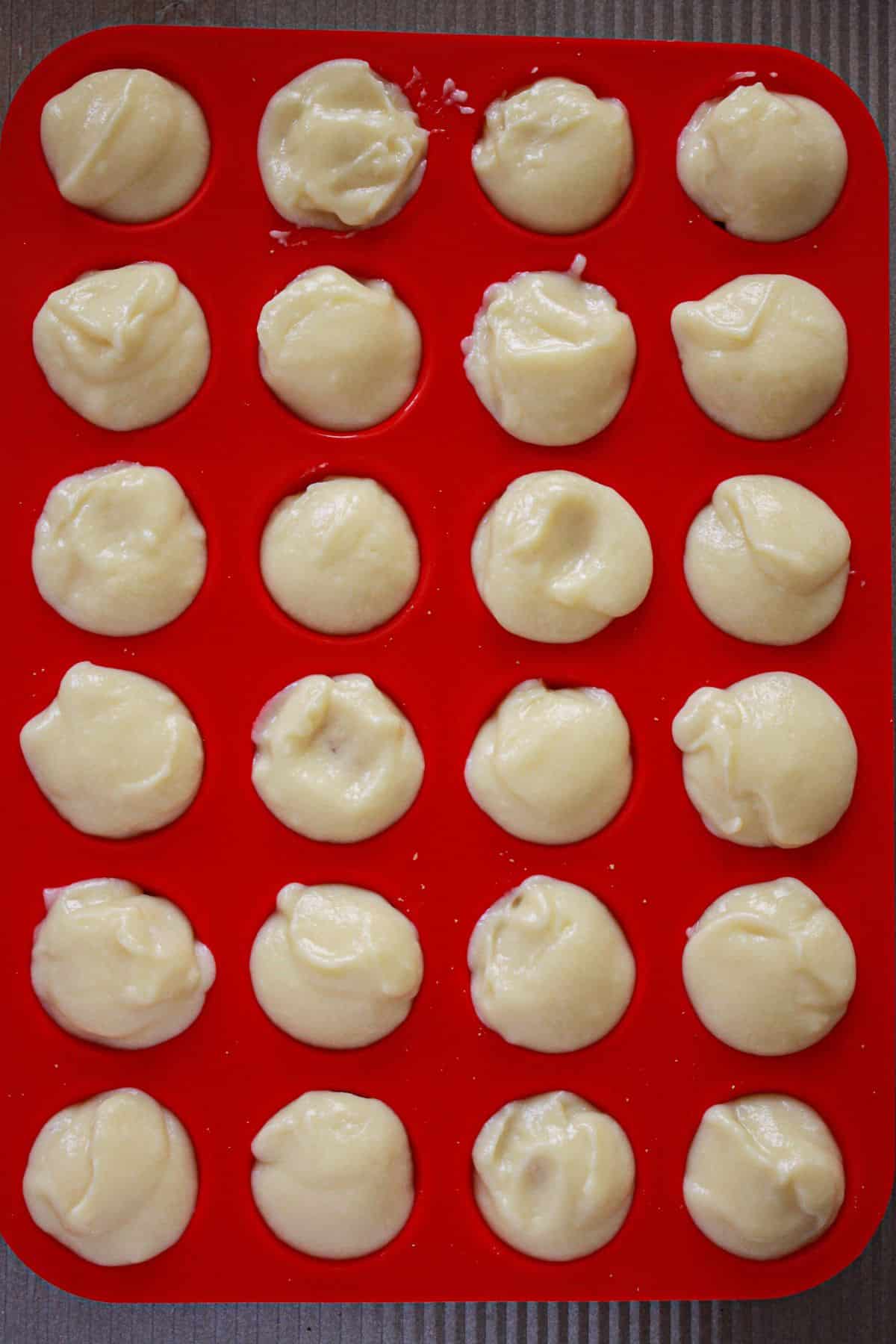 homemade custard being added to the top of a vanilla wafer in a silicone muffin pan.