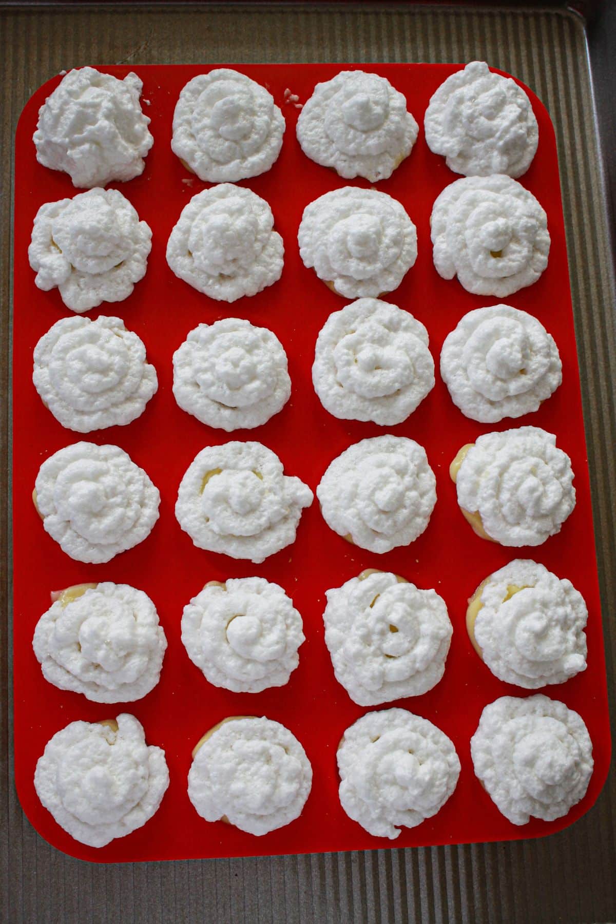 meringue being piped on top of banana pudding in a silicone mini muffin pan