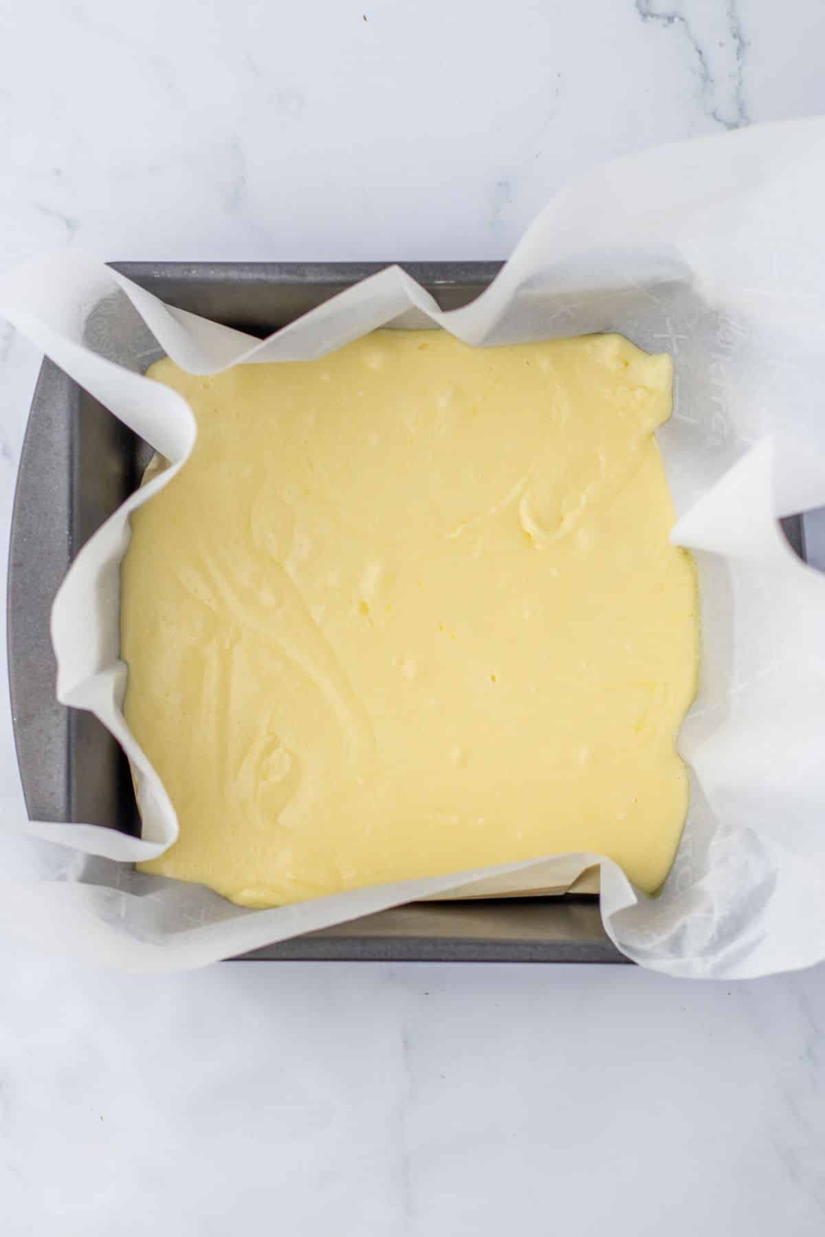 cream fudge layer being spread into a parchment lined square baking dish.