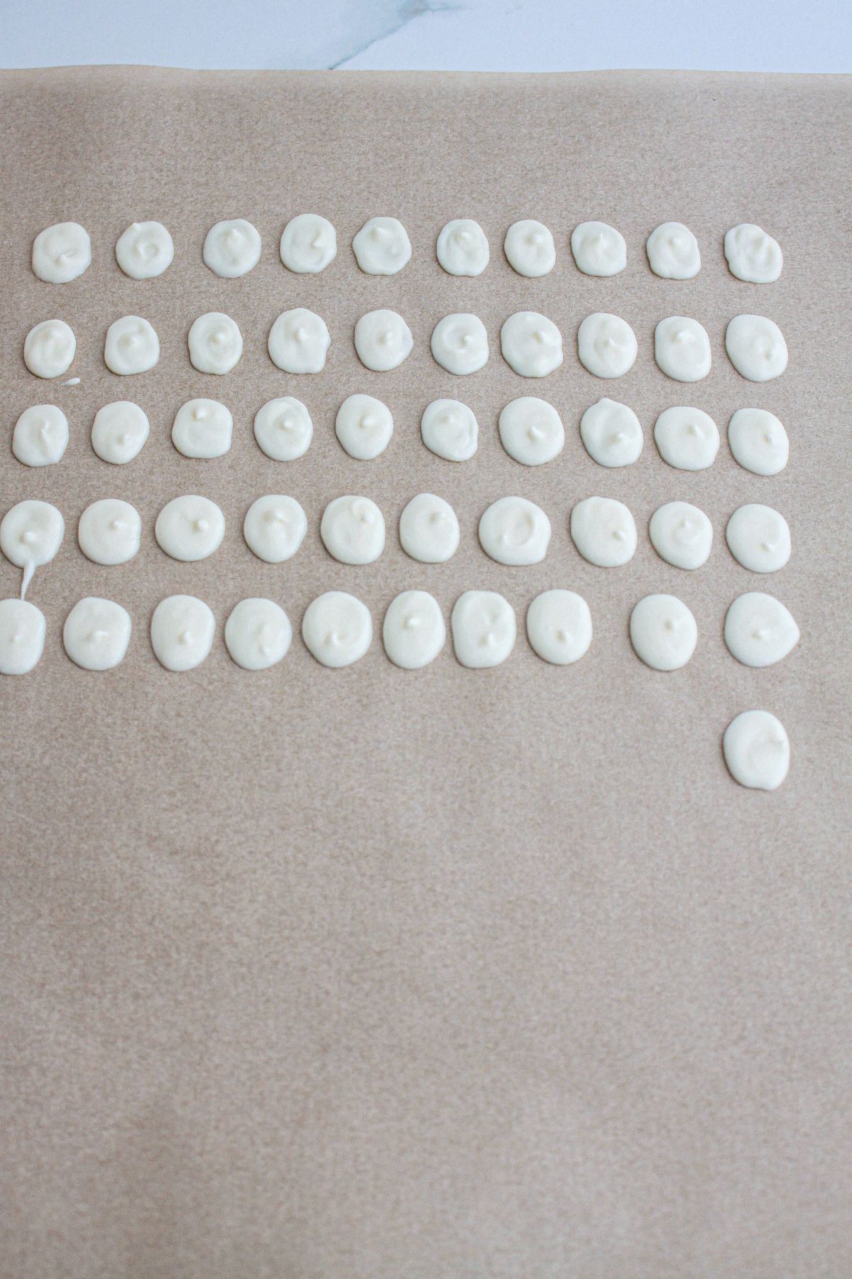 white chocolate ovals being piped onto a parchment lined baking sheet.