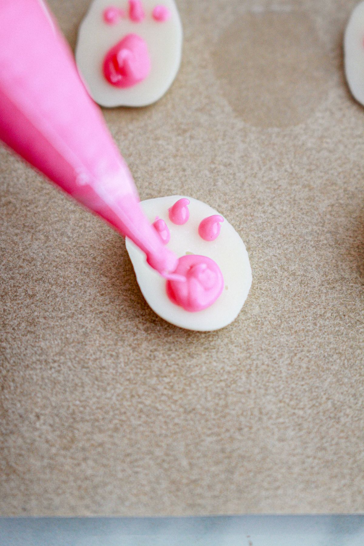 paws being piped on white chocolate on a parchment lined baking sheet.