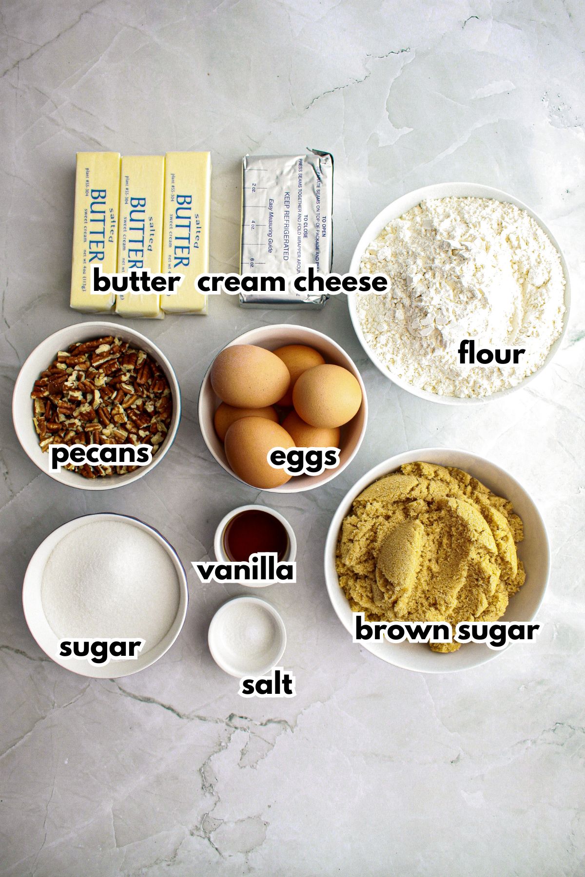 butter, cream cheese, flour, pecans, eggs, sugar, vanilla, salt, and brown sugar on a counter.