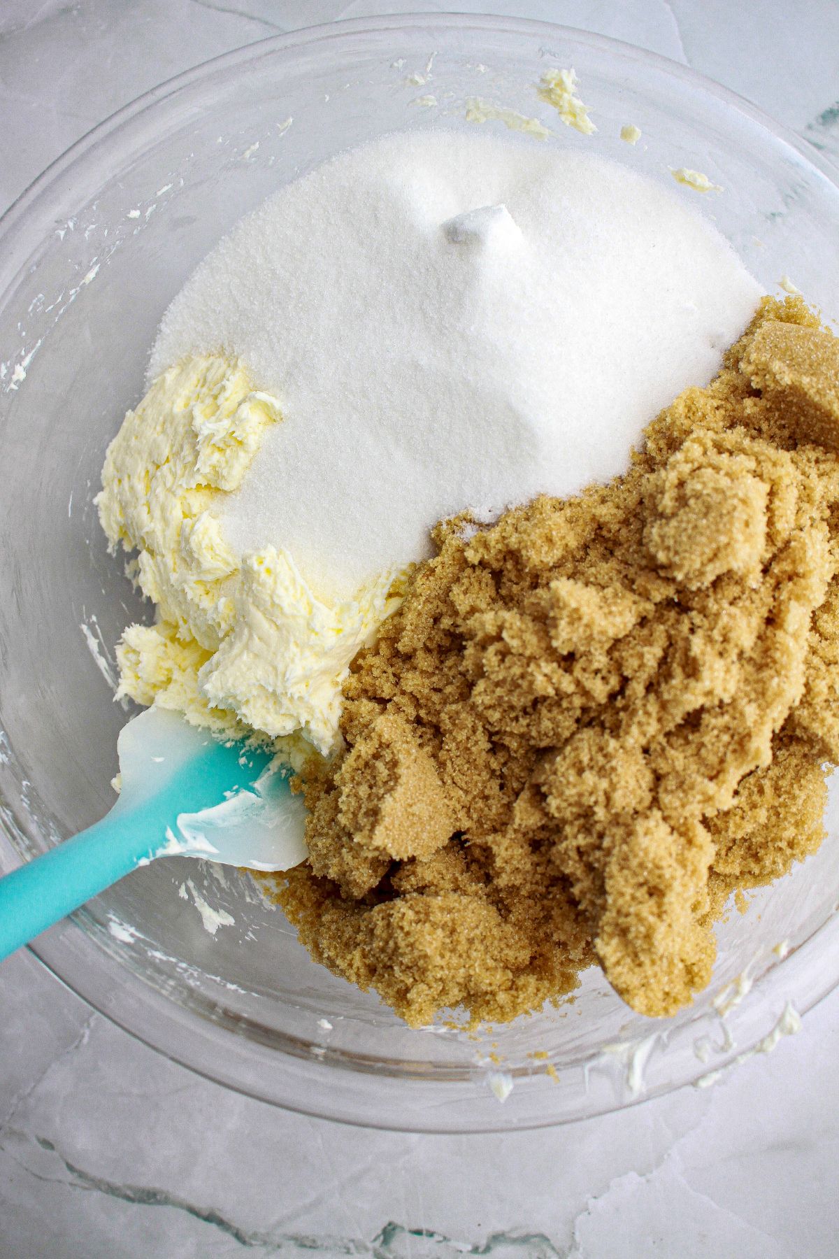 butter, sugar, and brown sugar being mixed in a glass mixing bowl.