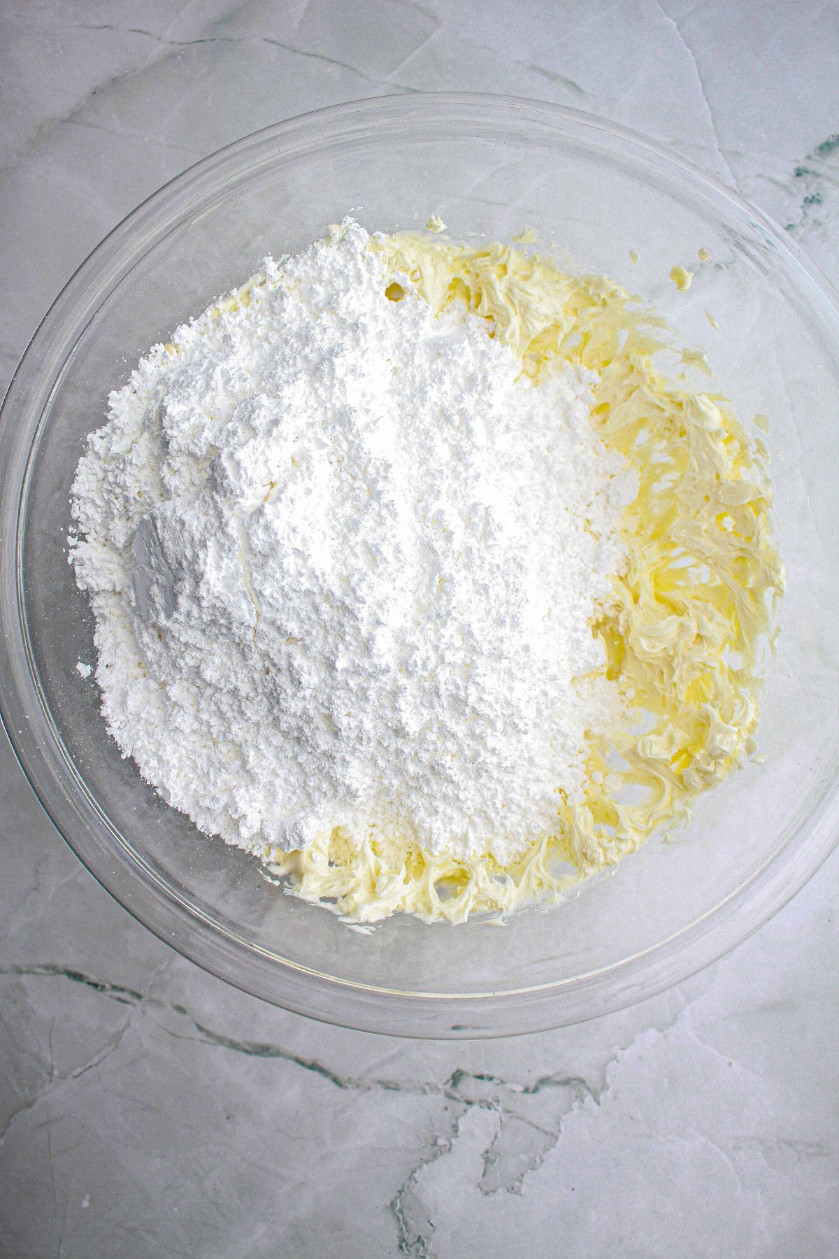 powdered sugar being added to a bowl of butter.