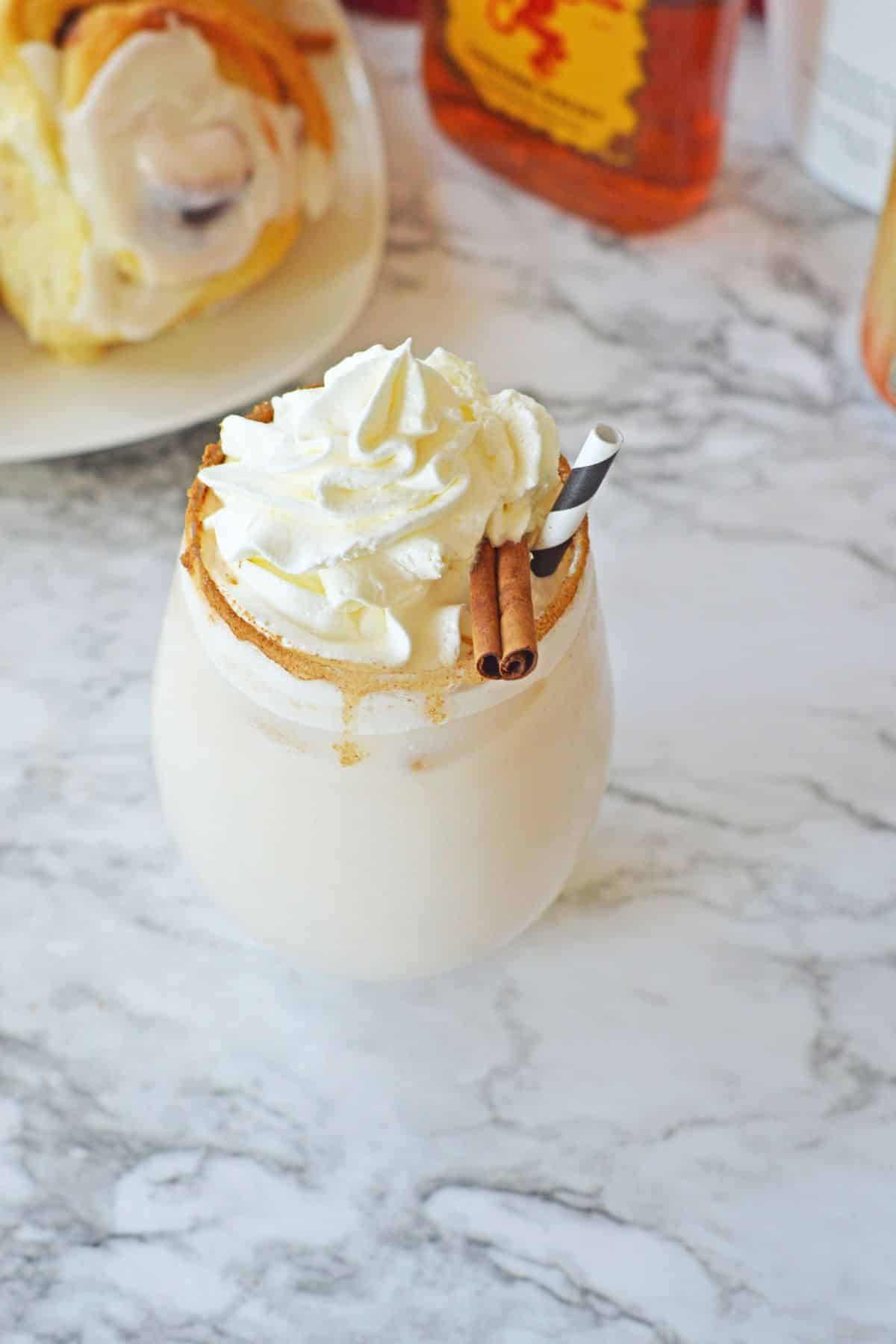 cinnamon roll cocktail on a marble counter topped with whipped cream and a cinnamon stick.