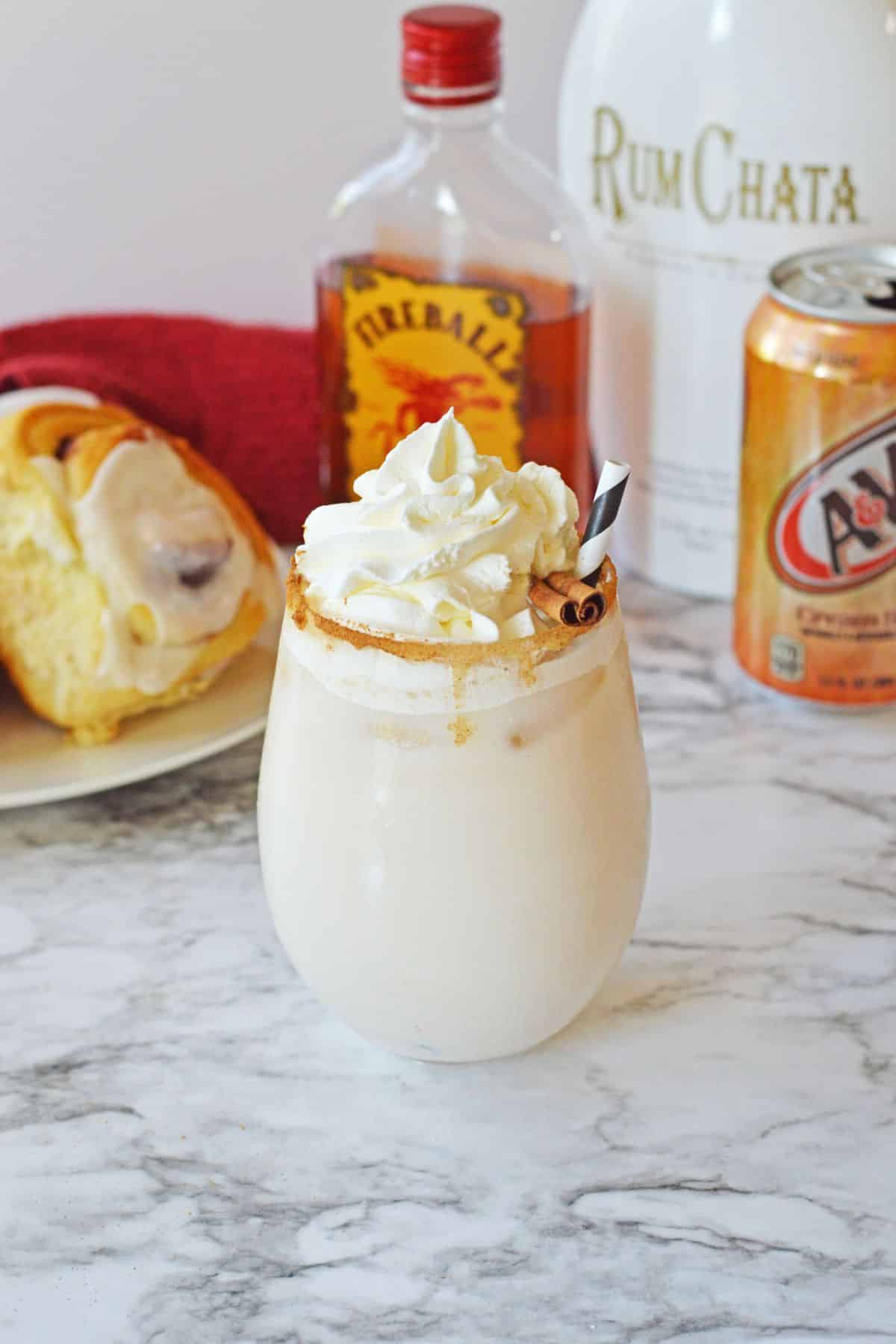 cinnamon roll cocktail on a marble counter topped with whipped cream and a cinnamon stick.