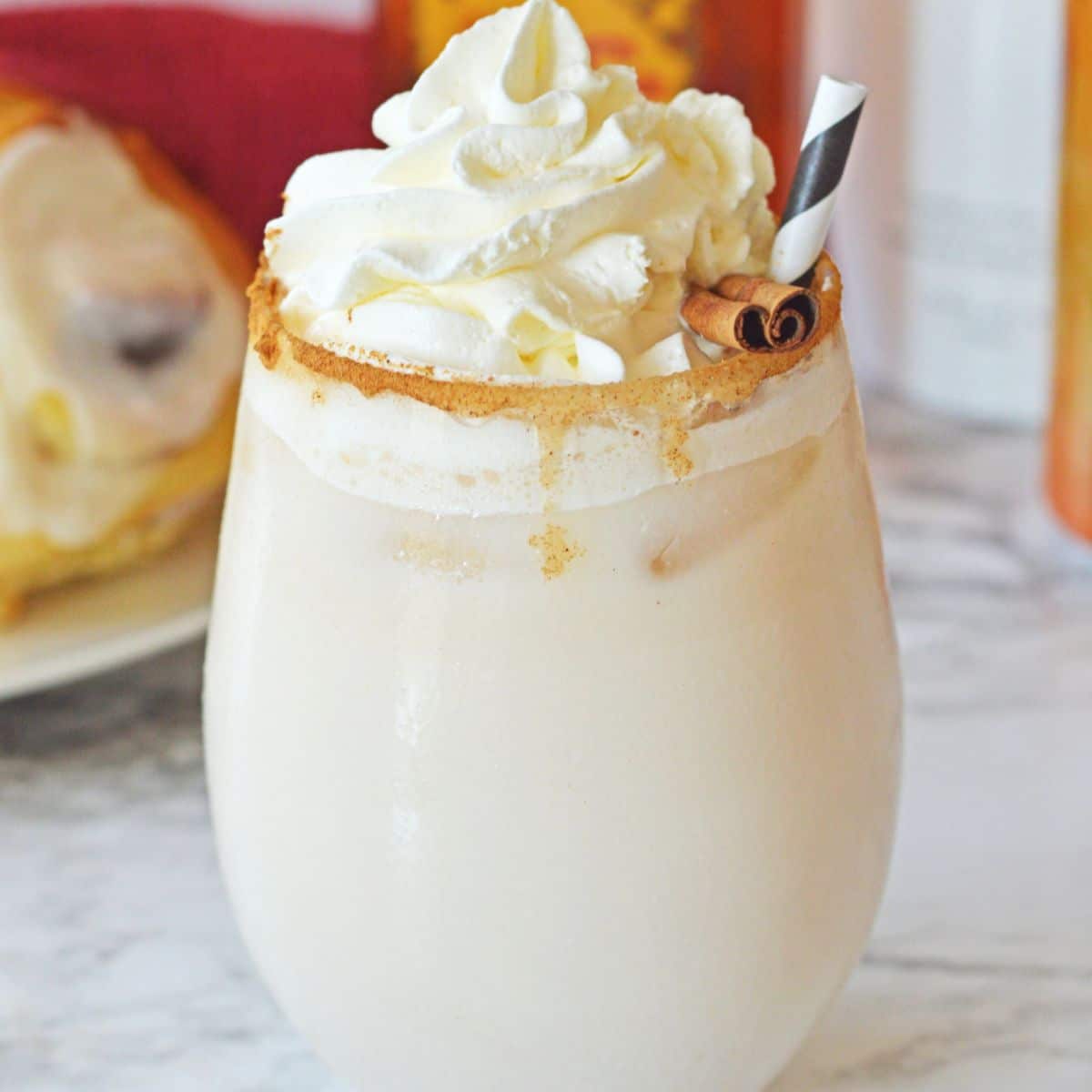 cinnamon roll cocktail on a marble counter topped with whipped cream and a cinnamon stick.