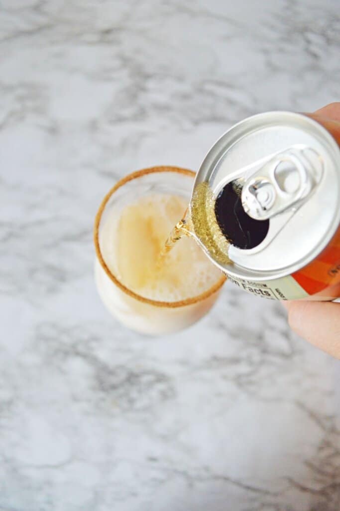 cream soda being poured into a cinnamon rimmed cocktail glass